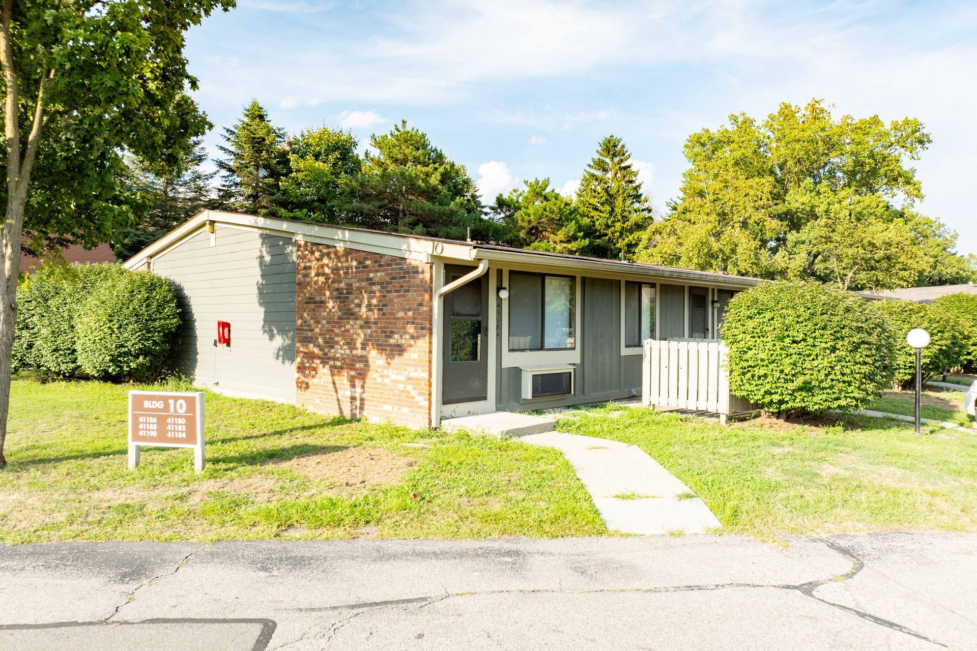 Single-story apartment building with faded exterior. Grass and pathway in front. Sunny day.
