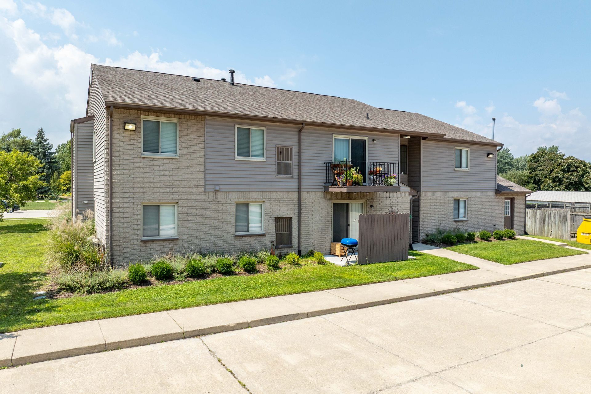 Apartment building exterior with brick and gray siding, green lawn, and blue sky.