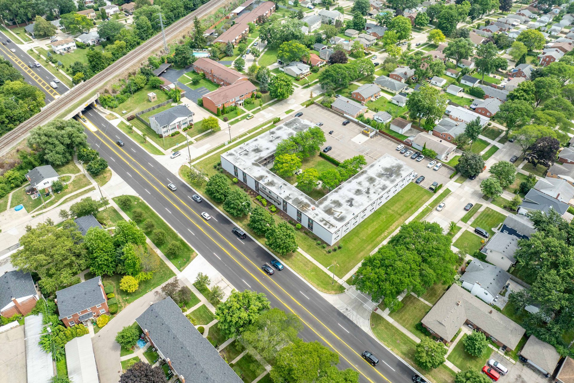 Aerial view of a suburban neighborhood with buildings, trees, and a multi-lane road.
