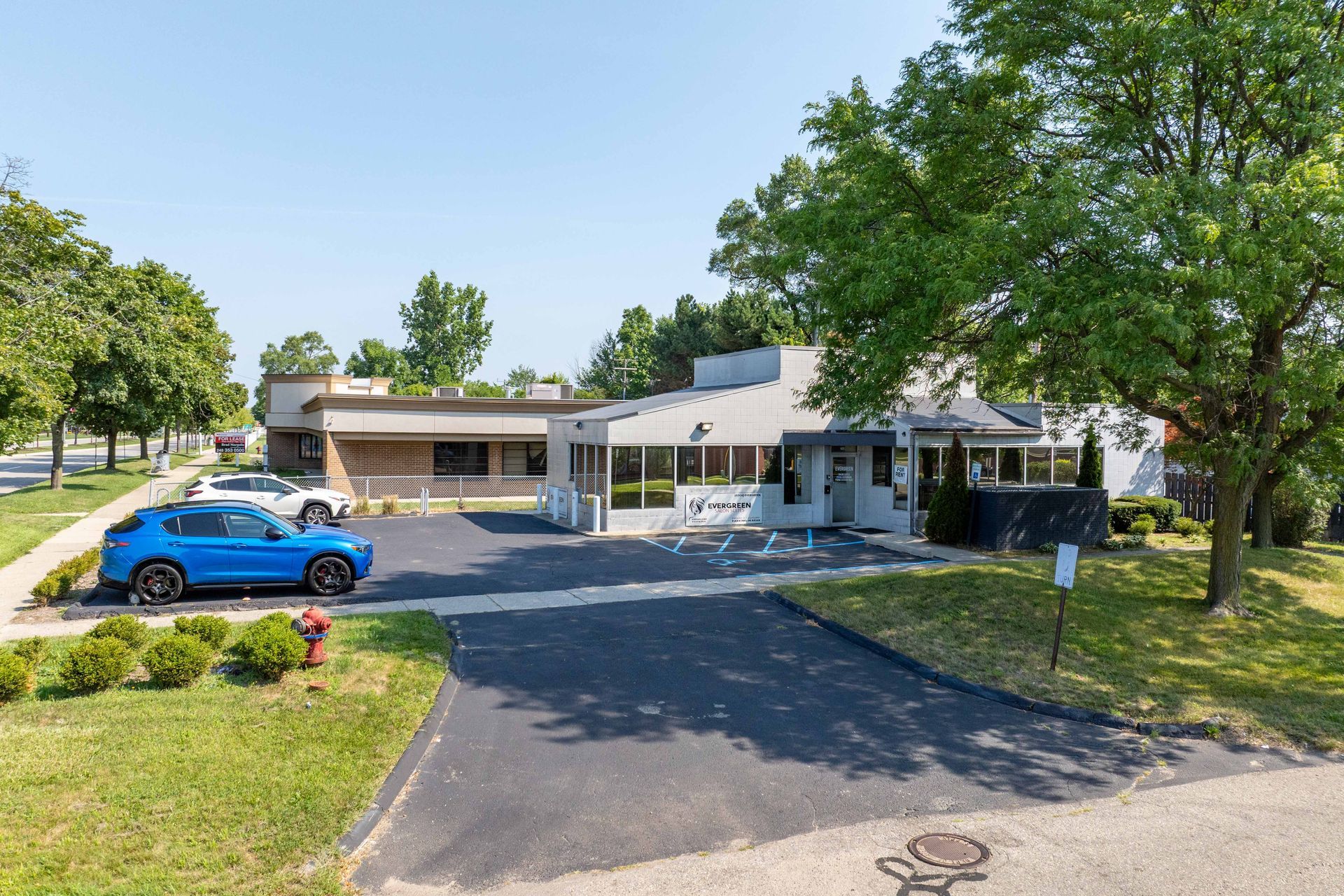 Blue SUV parked in front of a light-colored building with a paved driveway and grassy lawn, under a blue sky.