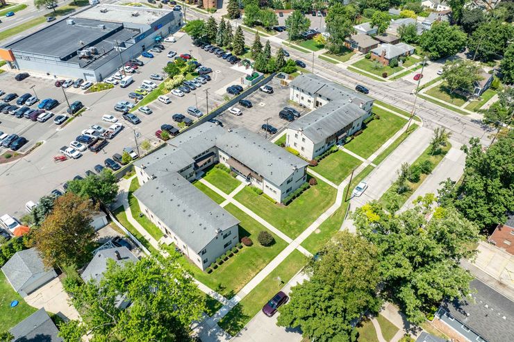 Aerial view of a U-shaped apartment complex with green lawns and a nearby parking lot filled with cars.