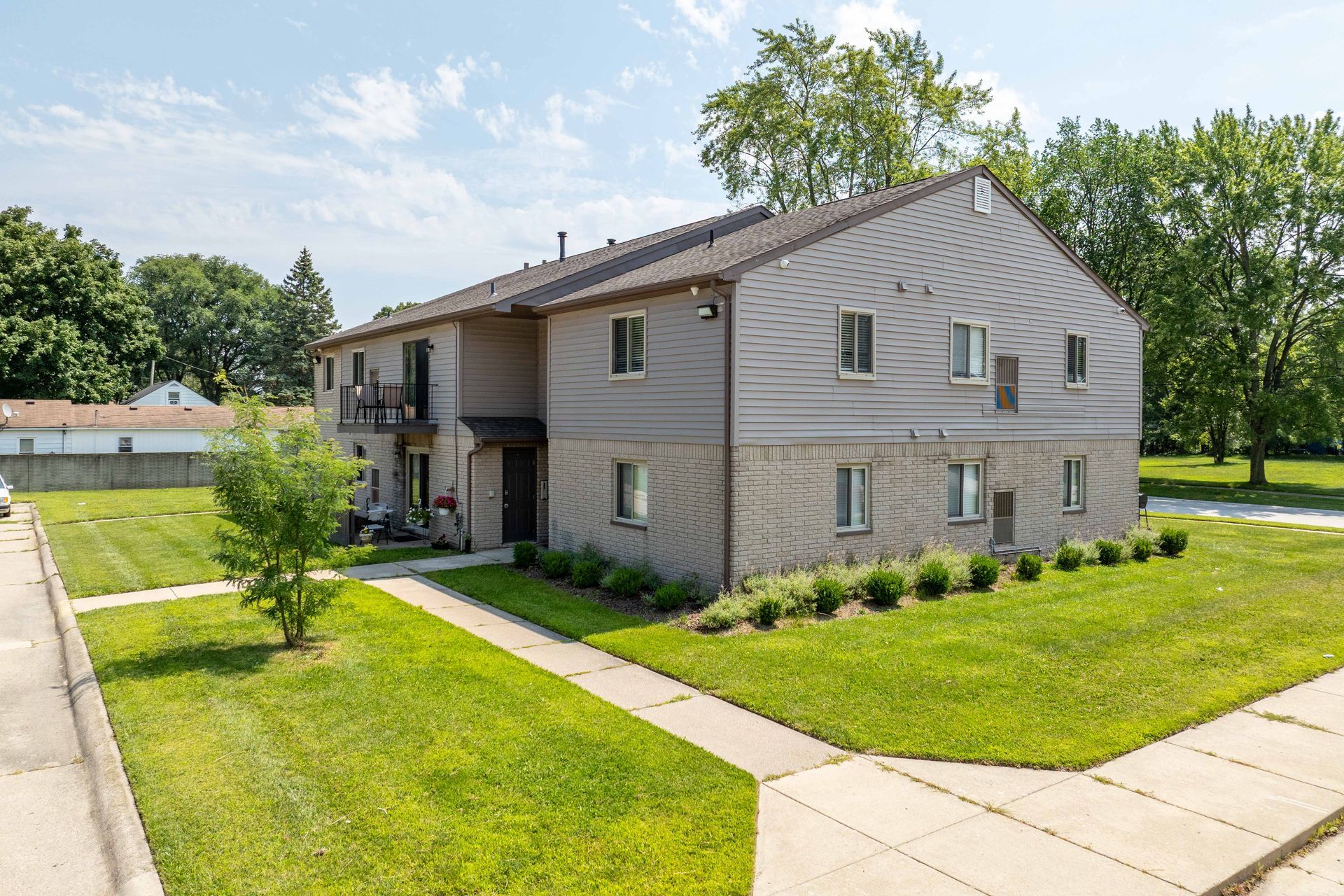 Two-story gray brick and siding apartment building on a grassy lot, sunny day.