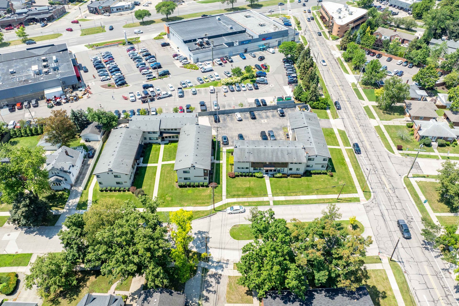 Aerial view: apartment complex surrounded by green lawns, a road, and other buildings.