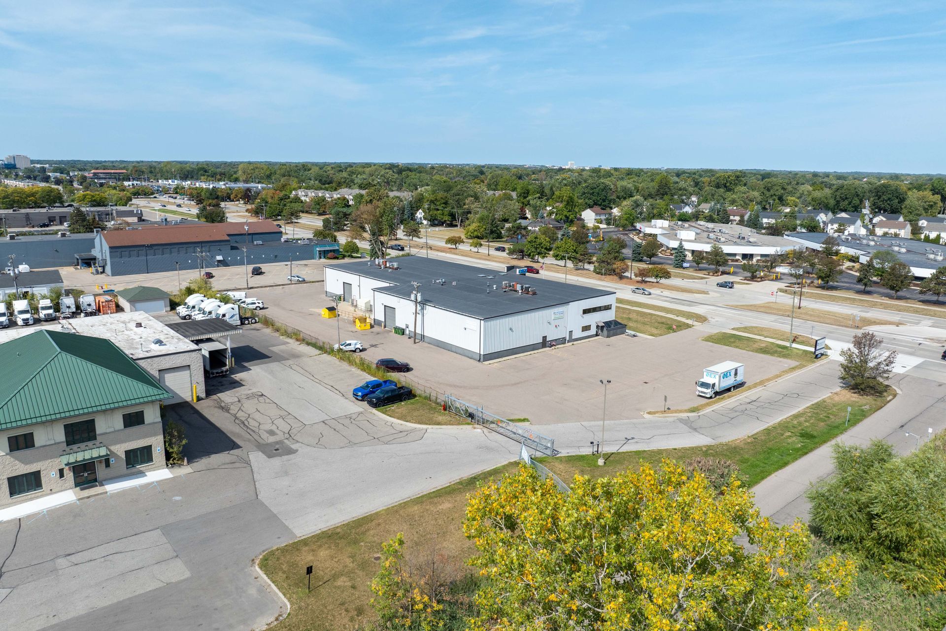 Aerial view of commercial buildings with parking, under a blue sky, trees in the background.