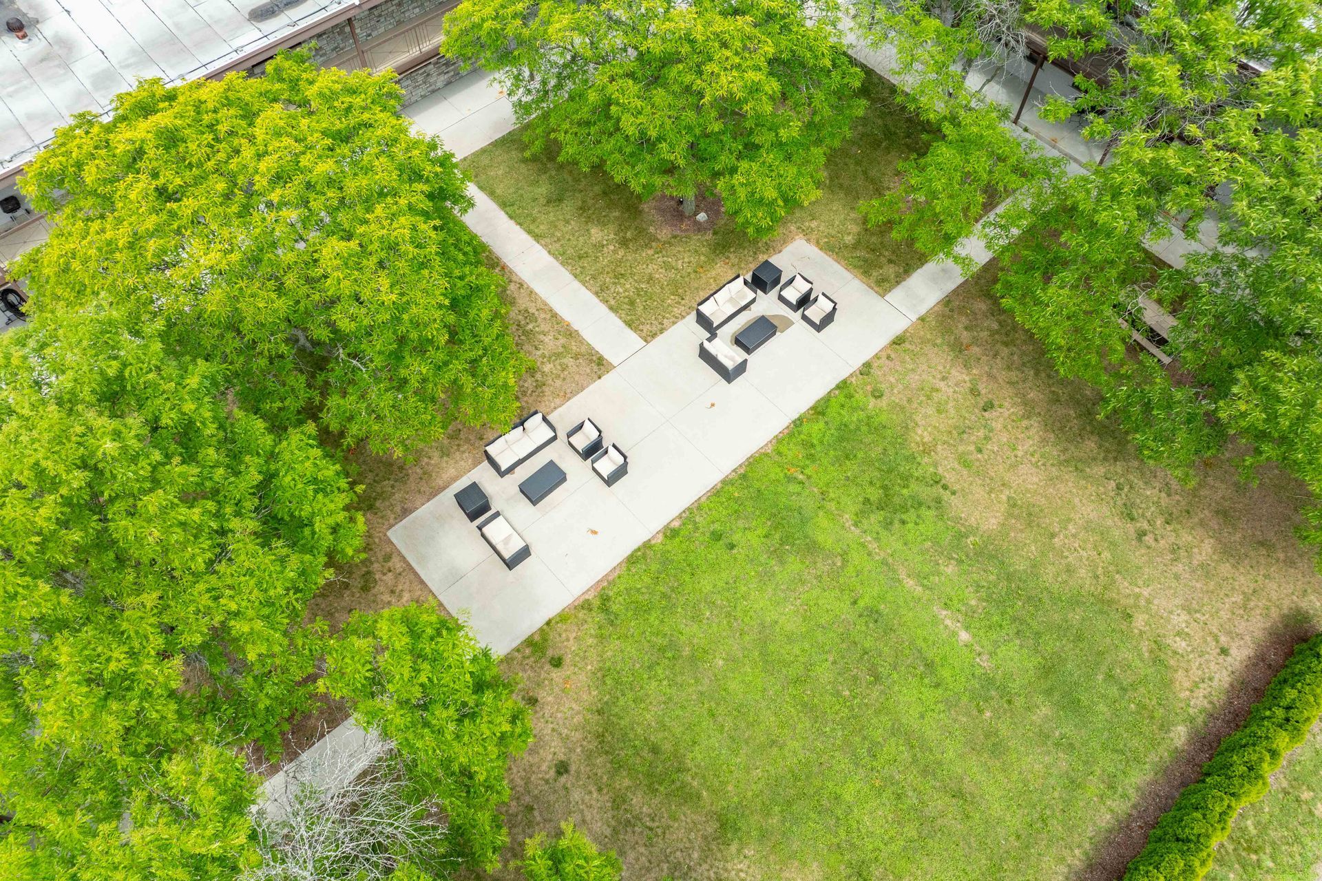 Overhead view of outdoor lounge area with seating on a concrete path surrounded by green trees and grass.