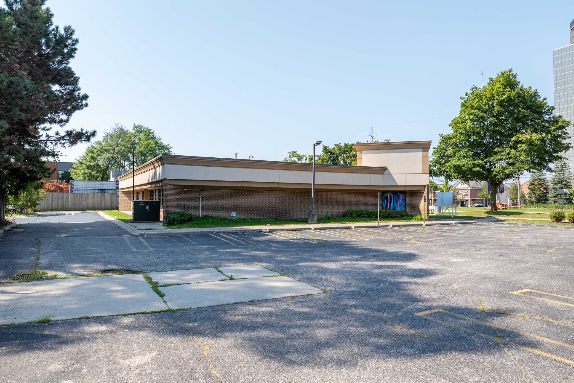 Exterior view of a vacant, brown single-story building and empty parking lot on a sunny day.