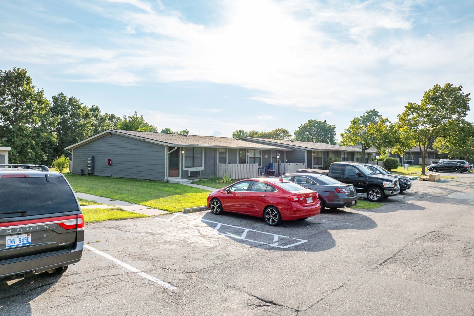 Parking lot with cars in front of low-rise gray buildings on a sunny day.