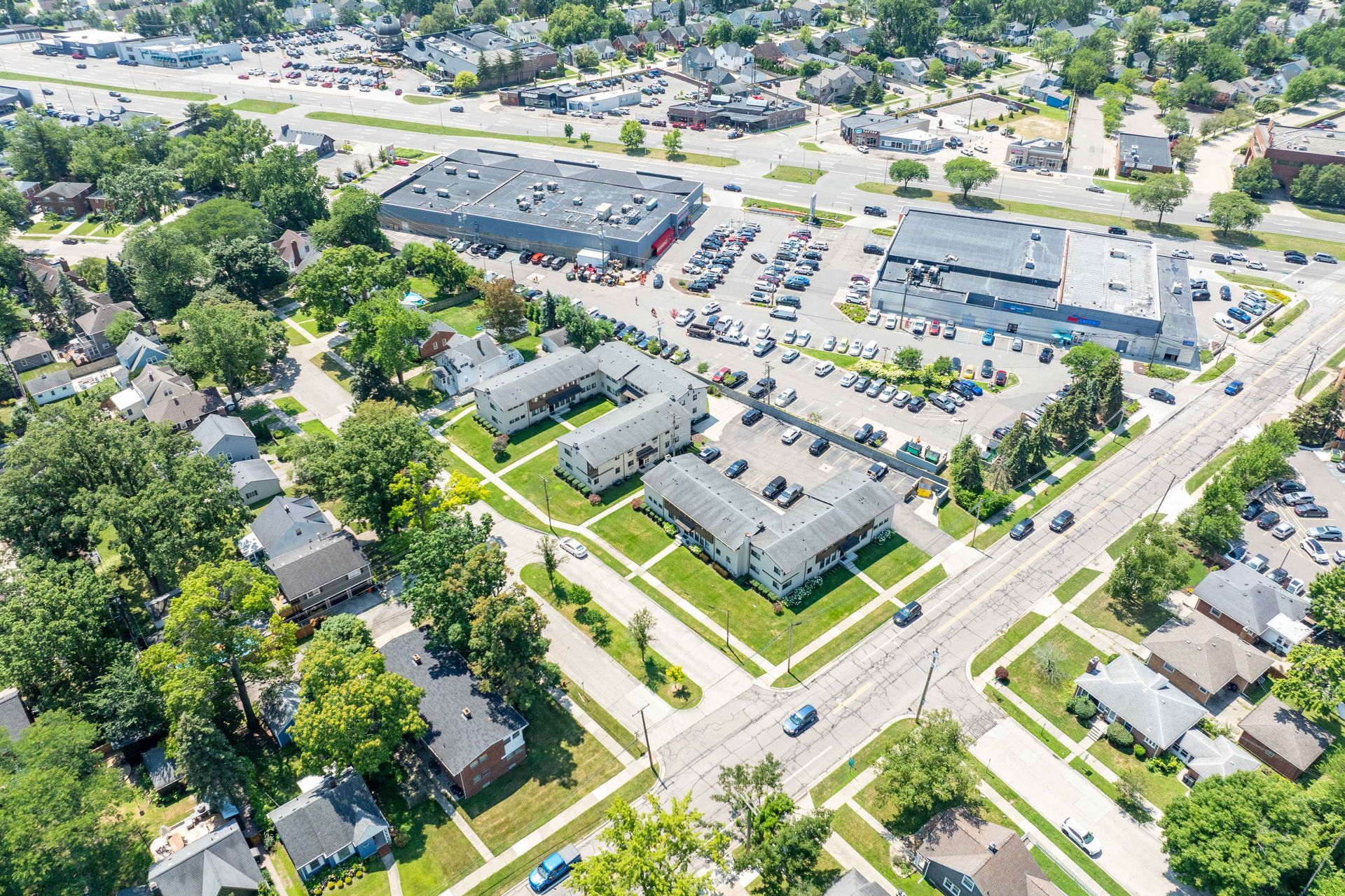 Aerial view: buildings with parking lots, residential homes, and trees in a suburban area on a sunny day.