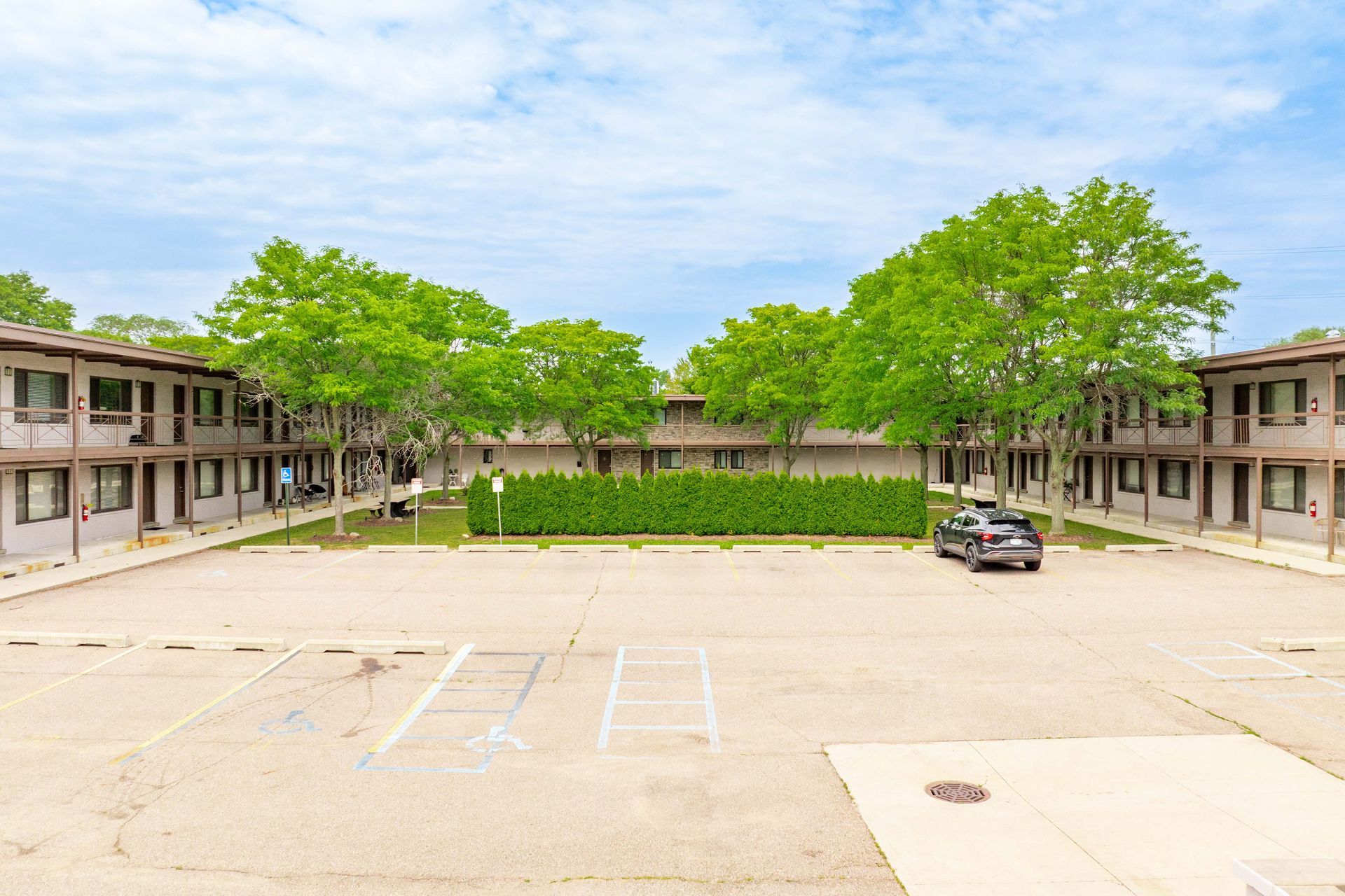 Apartment complex with parking area and green trees under a cloudy sky.