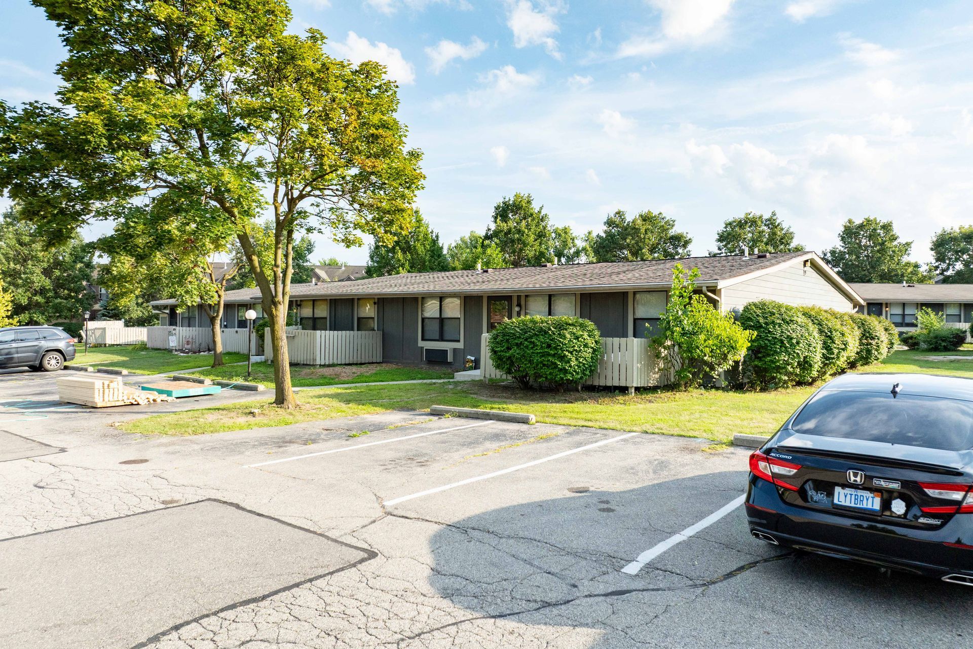 Gray apartment building with cars parked out front on a sunny day.