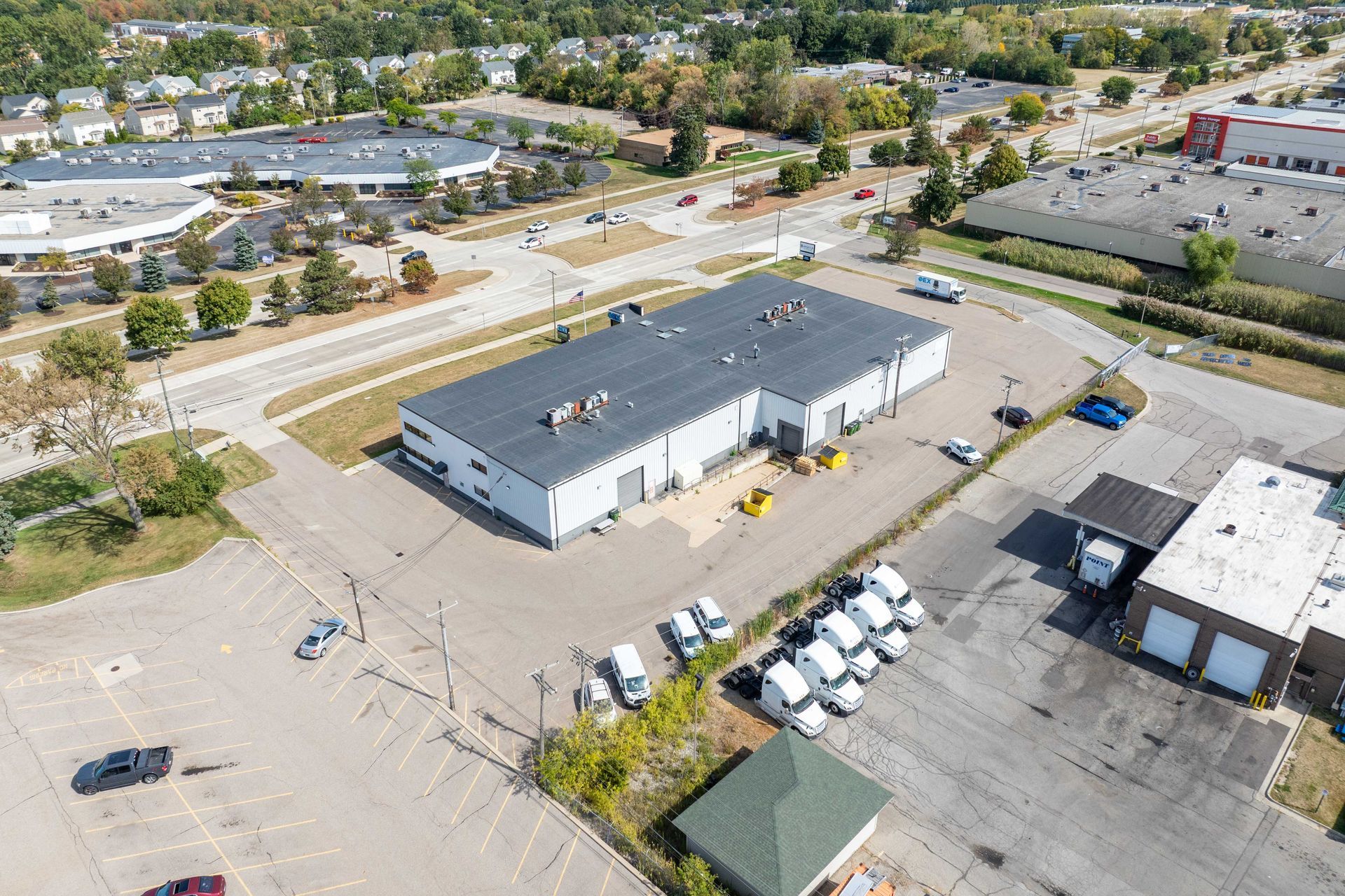 Aerial view of an industrial building with a flat roof and loading docks, surrounded by parking and a road.