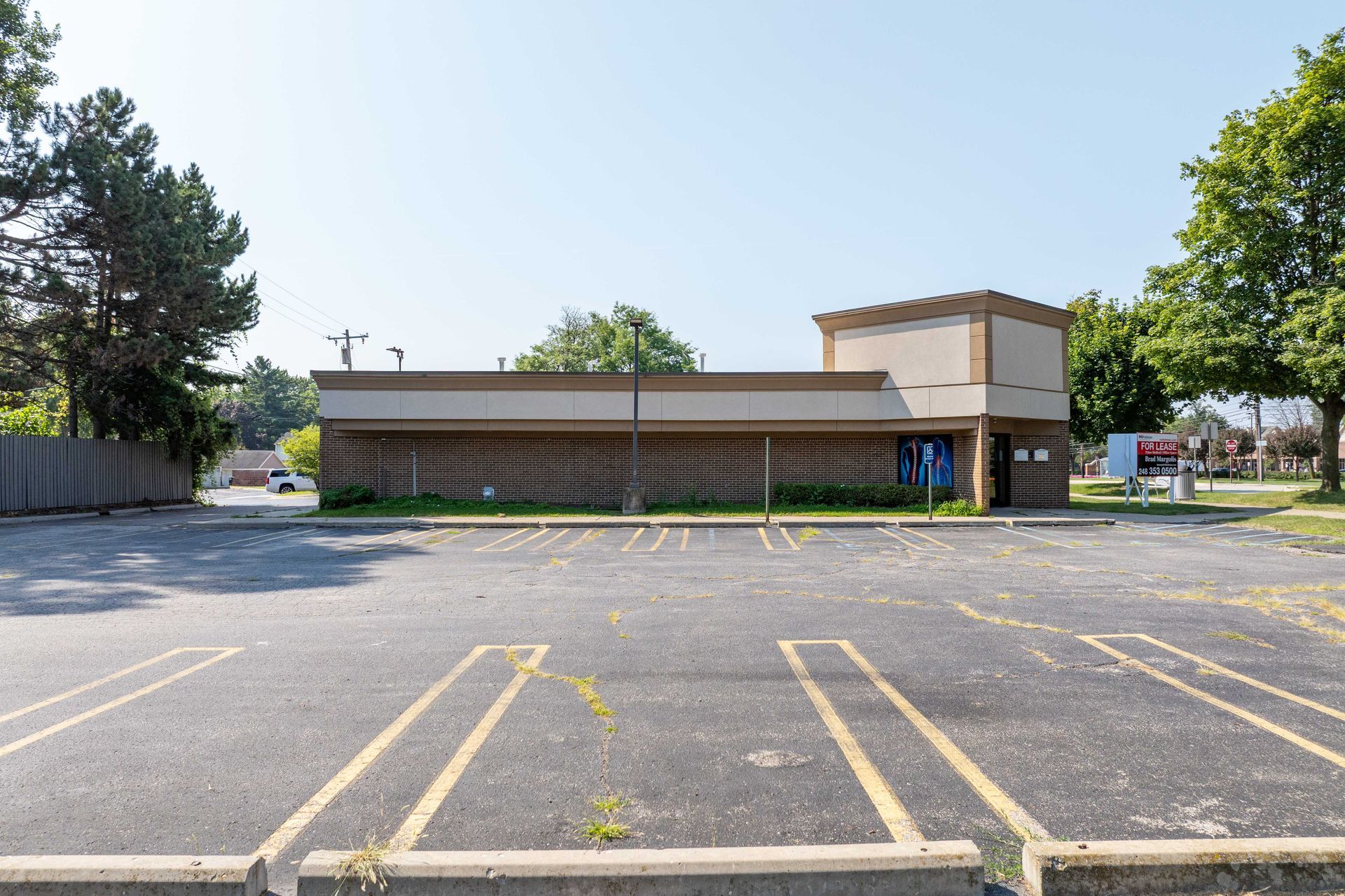 Abandoned one-story building with a cracked asphalt parking lot. Beige facade, overgrown weeds.