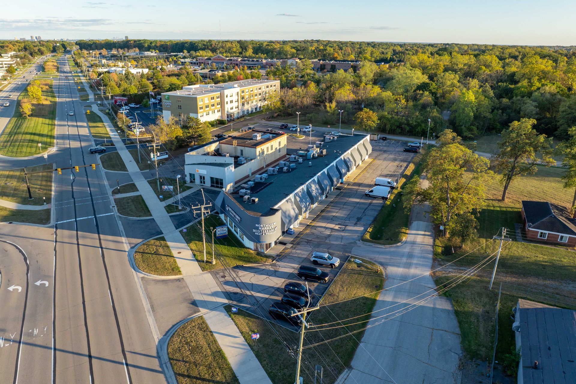 Aerial view of a unique, curved building with parked cars, surrounded by roads and trees.