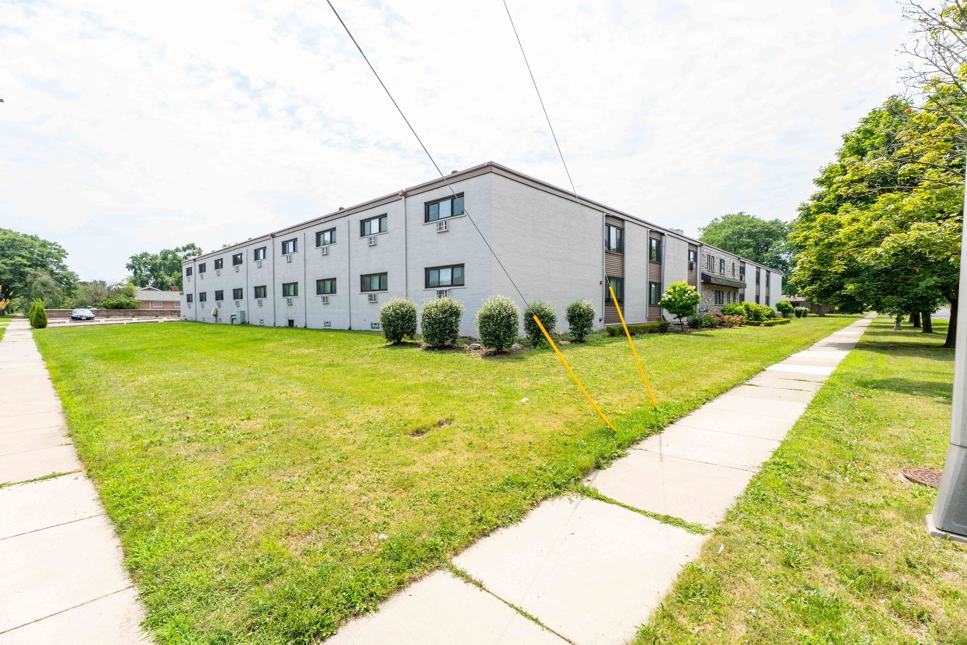 Two-story apartment building with green lawn and sidewalk, sunny day.