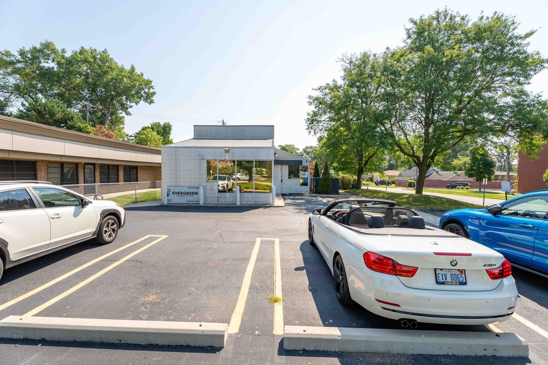 Parking lot with cars, building, trees. White convertible parked in front.
