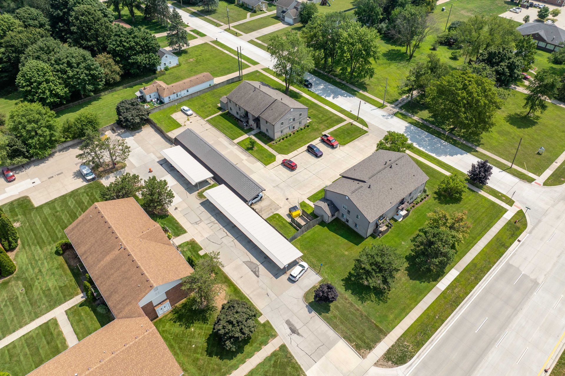 Aerial view of apartment buildings and covered parking in a grassy neighborhood.