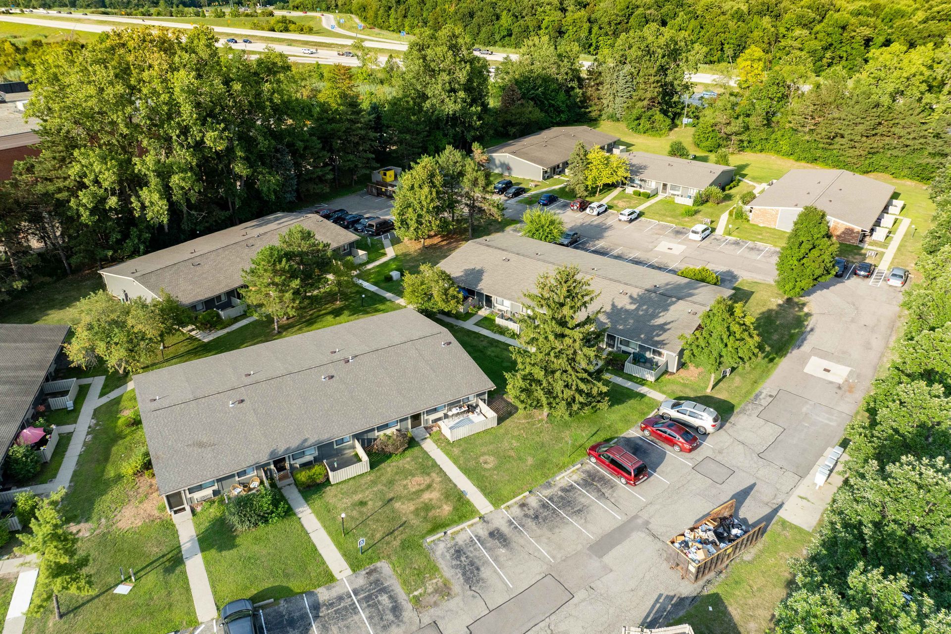 Aerial view of apartment complex with multiple buildings, trees, and parking areas.
