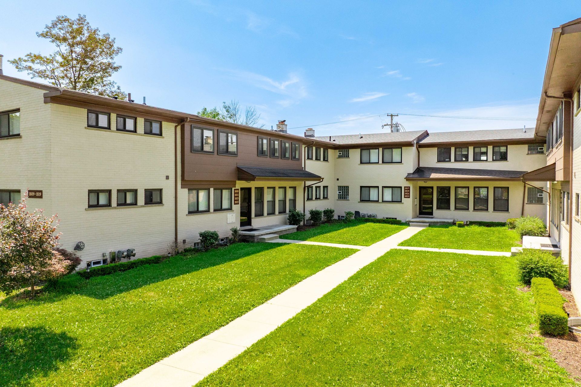 A two-story tan apartment building with a grass courtyard, blue sky, and a walkway.