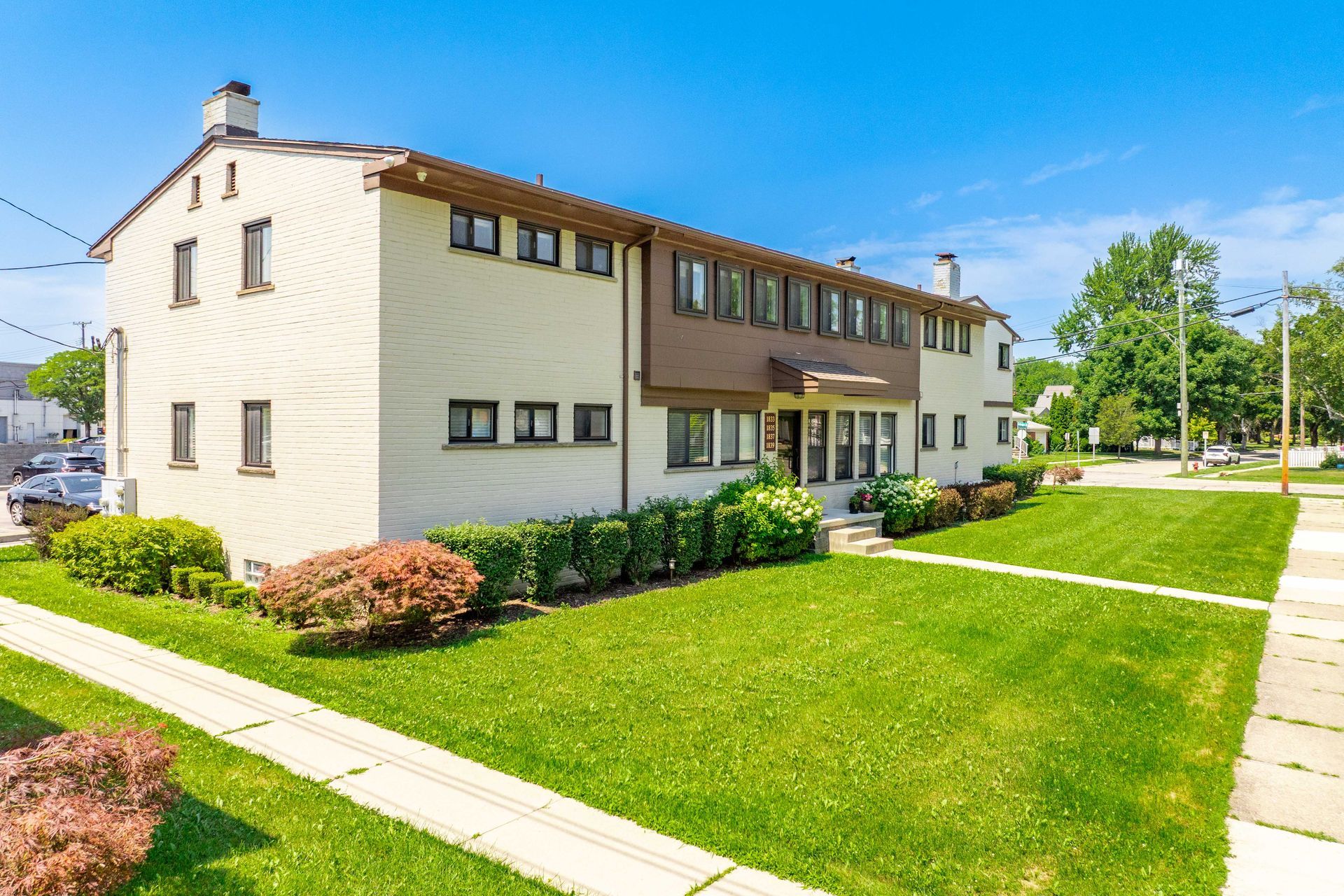 Two-story beige building with brown accents and green lawn on a sunny day.