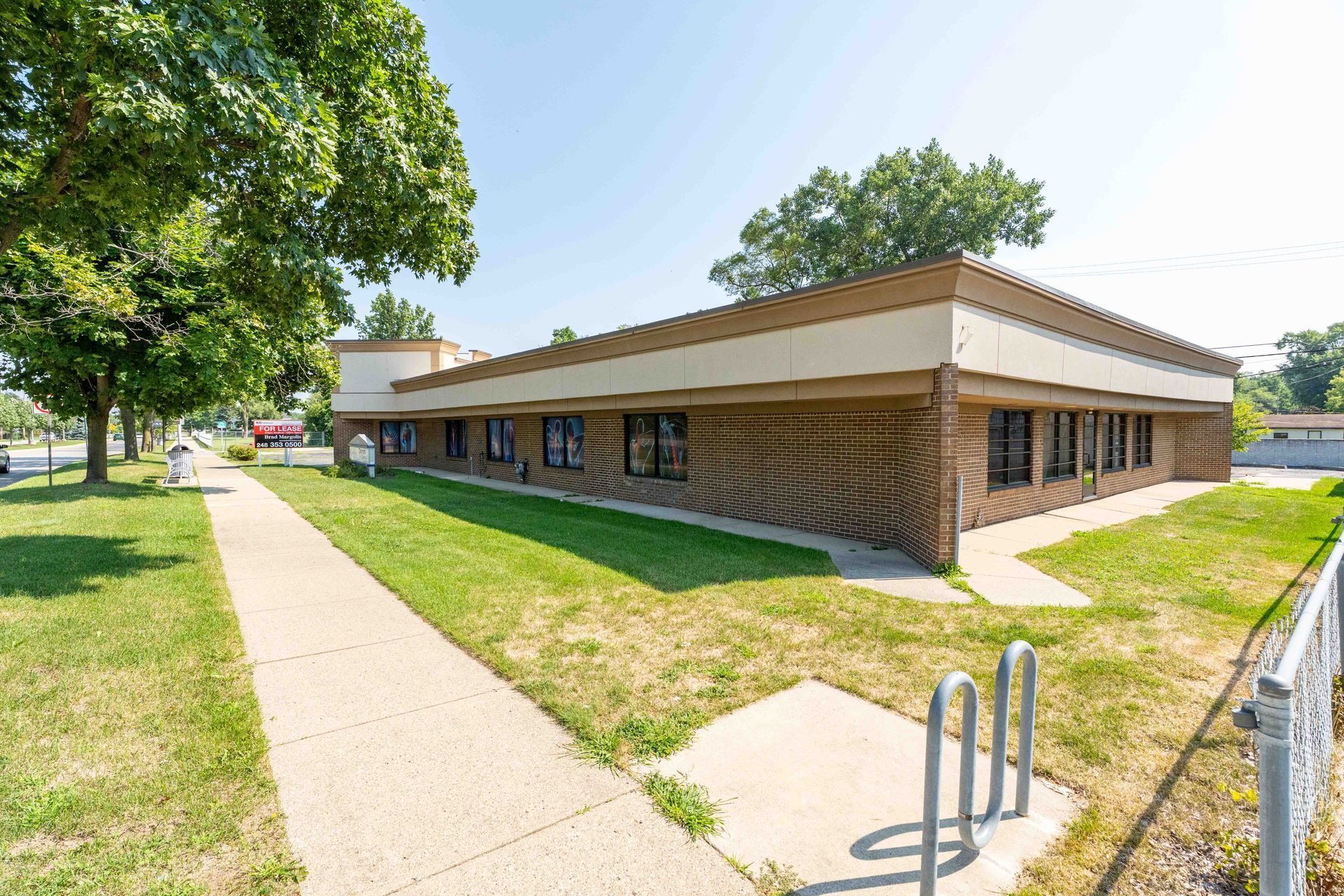 Office building with brick facade, sidewalk, and bike rack. Sunny day.