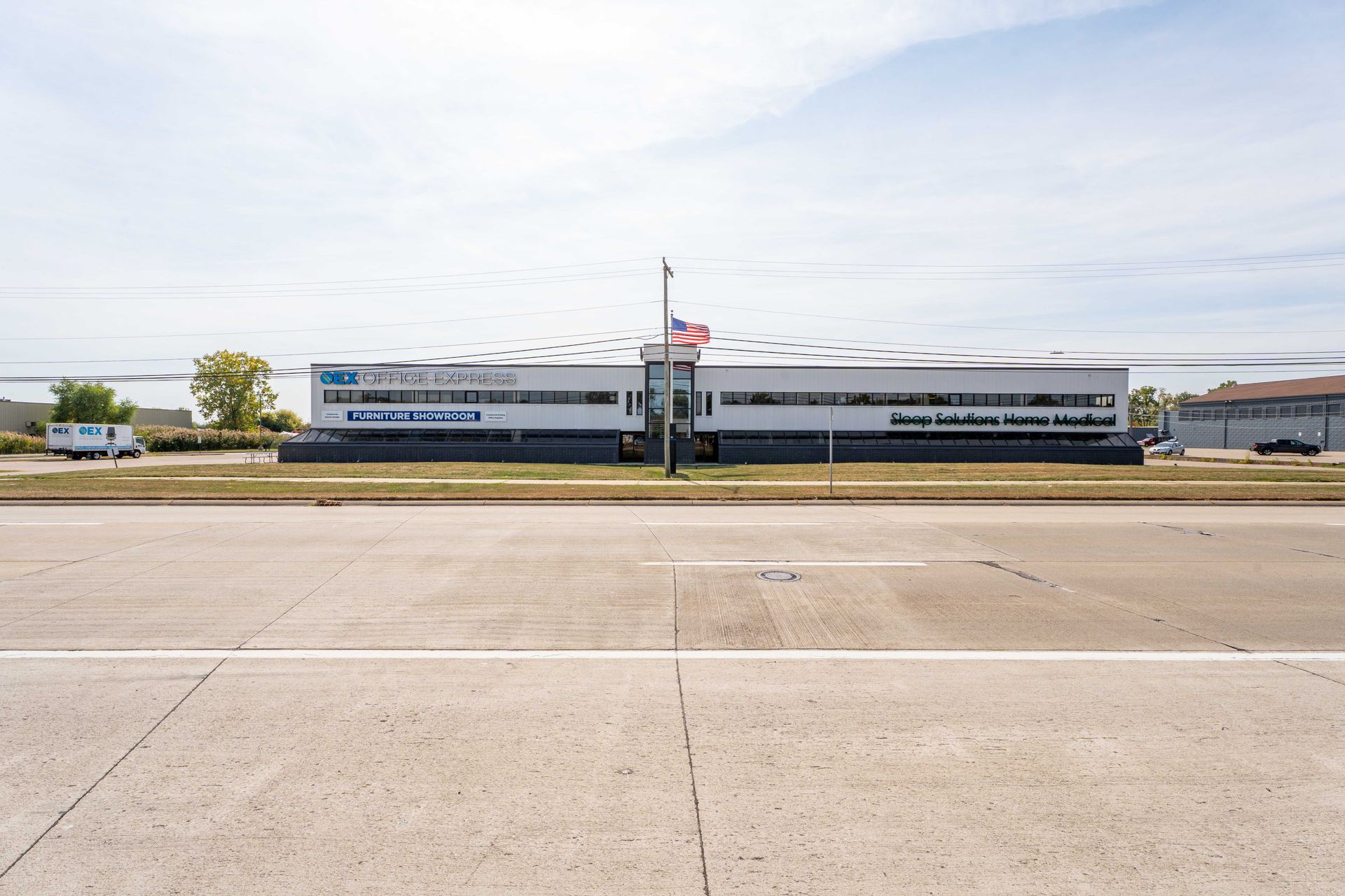A long, modern building with a blue sign and US flag, viewed from a highway.