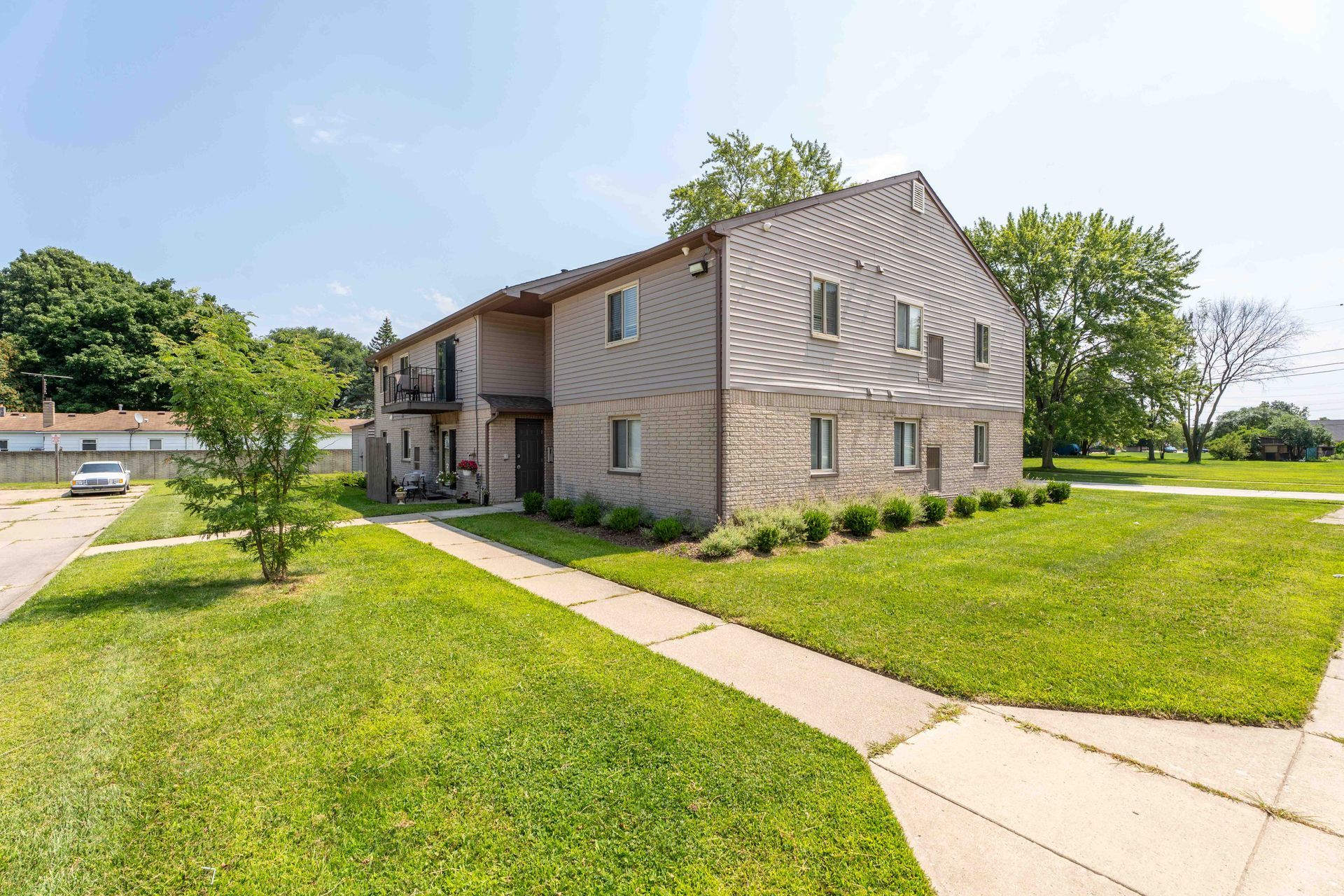 Two-story tan apartment building with green lawn and trees under a blue sky.