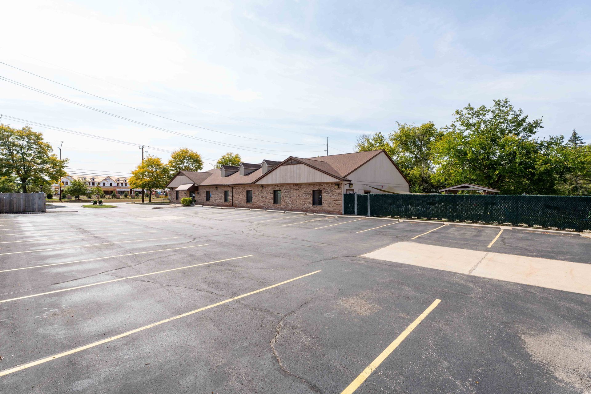 Empty parking lot in front of a low, brown brick building with a dark roof, under a blue sky.
