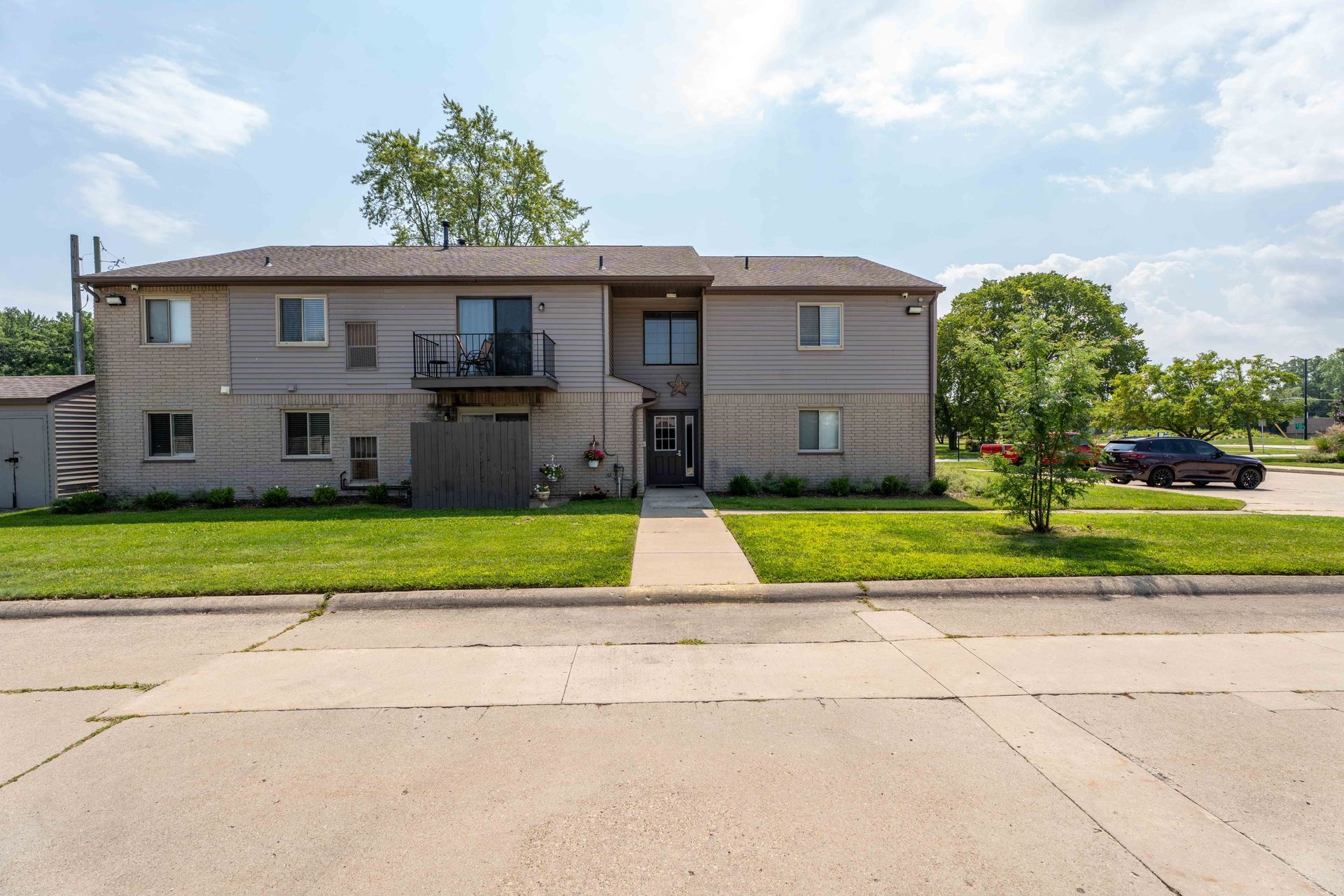 Two-story apartment building with light gray siding, balcony, and green lawn under a blue sky.
