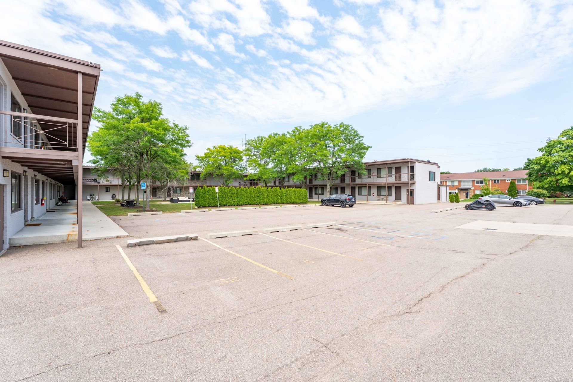 Gravel parking lot in front of two-story motel with trees and a bright, cloudy sky.