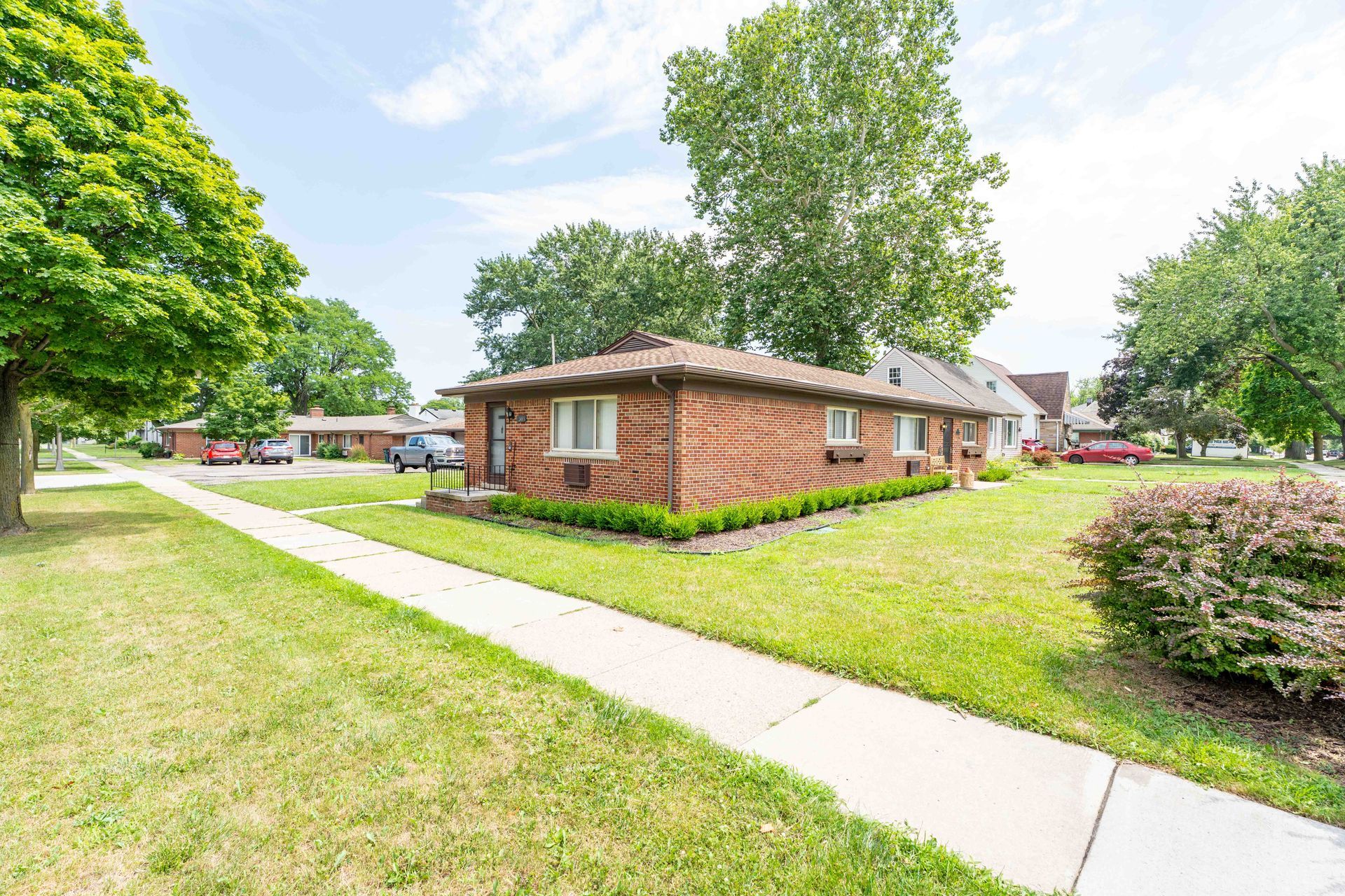 Brick house with green lawn and sidewalk, trees, and blue sky.