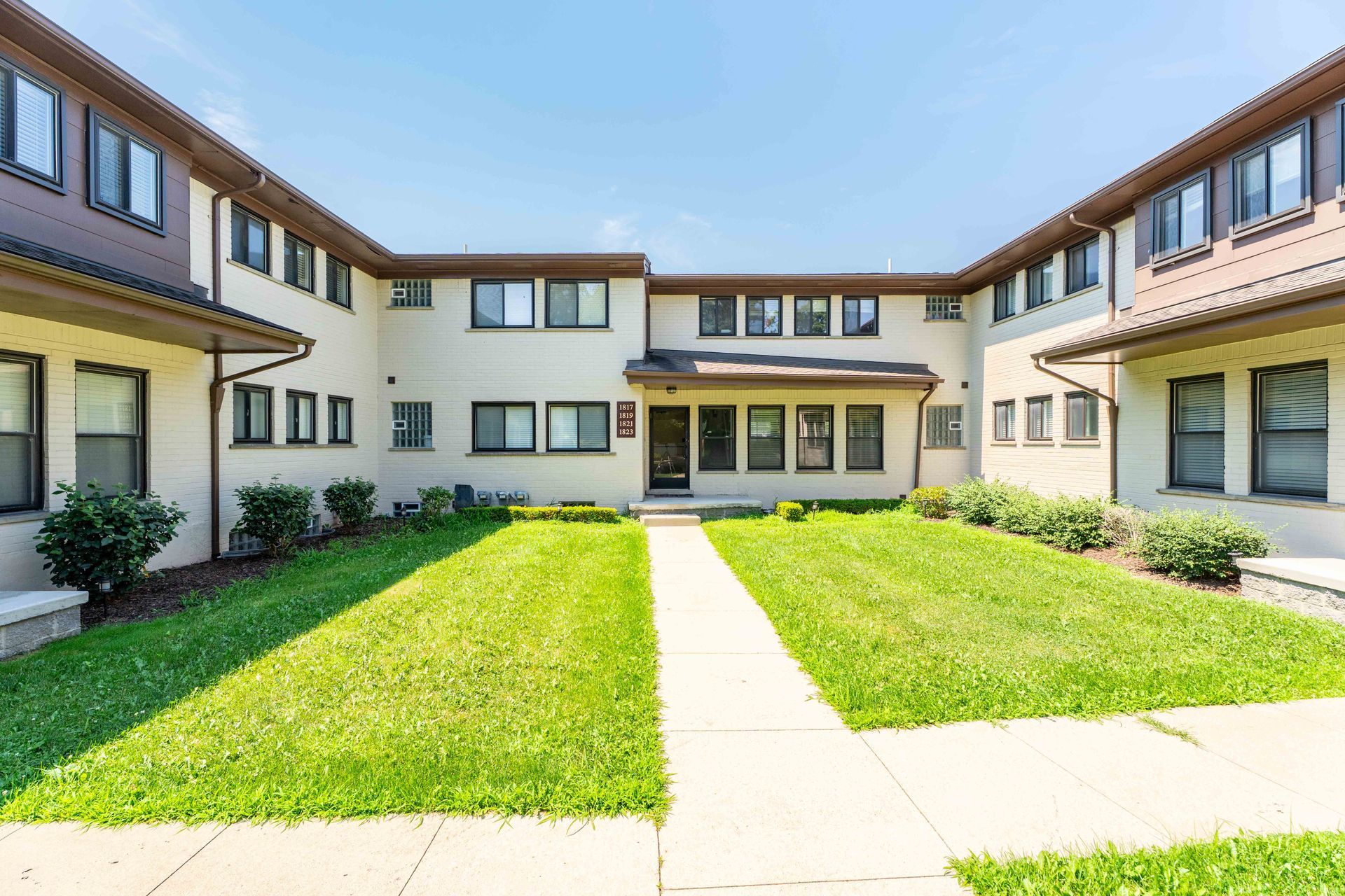 Townhouses with beige exterior, windows, and a grassy courtyard with a walkway.