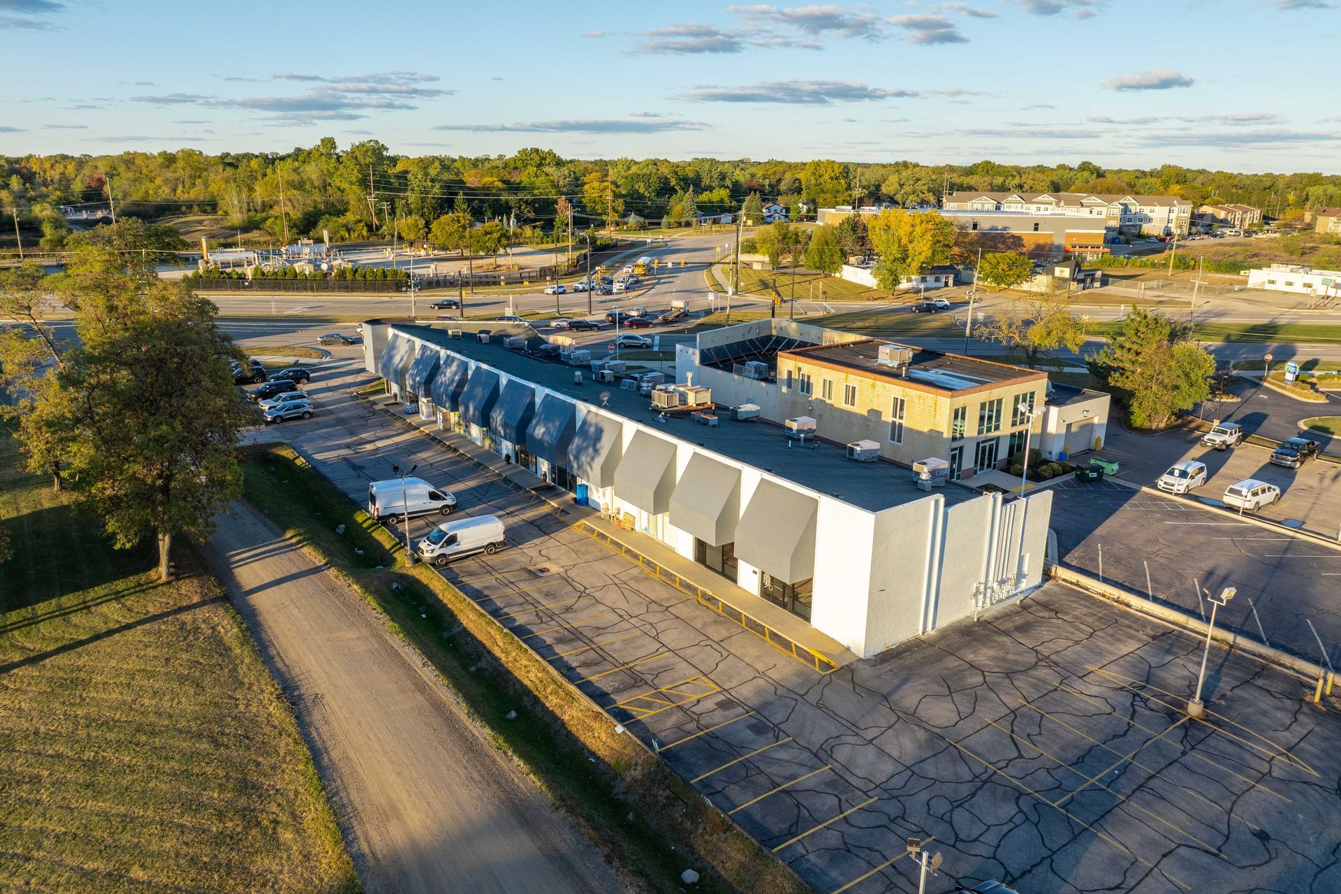 Aerial view of a long, gray commercial building with a parking lot and road in an urban area.