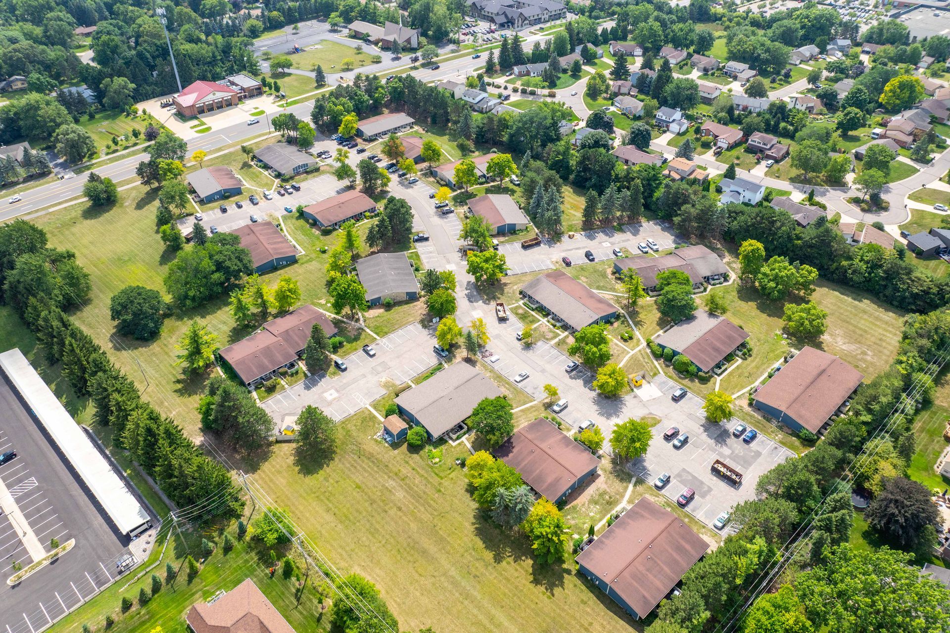 Aerial view of a residential area with brown-roofed buildings, green trees, and parking lots, in a suburban setting.