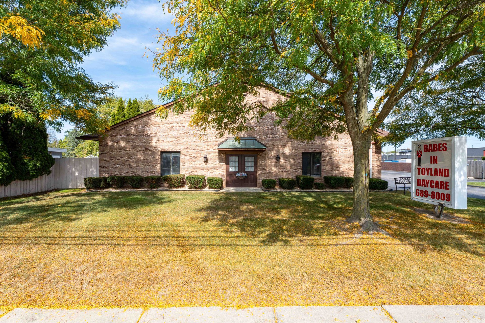 Brick building with a tree in front and a sign; 14 Taylor's Key & Lock Service, green and brown.