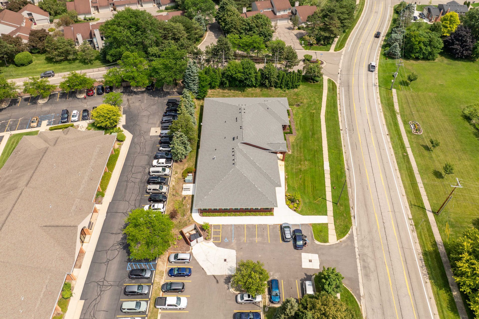 Aerial view of a building with a parking lot. Located near a road and surrounded by trees.