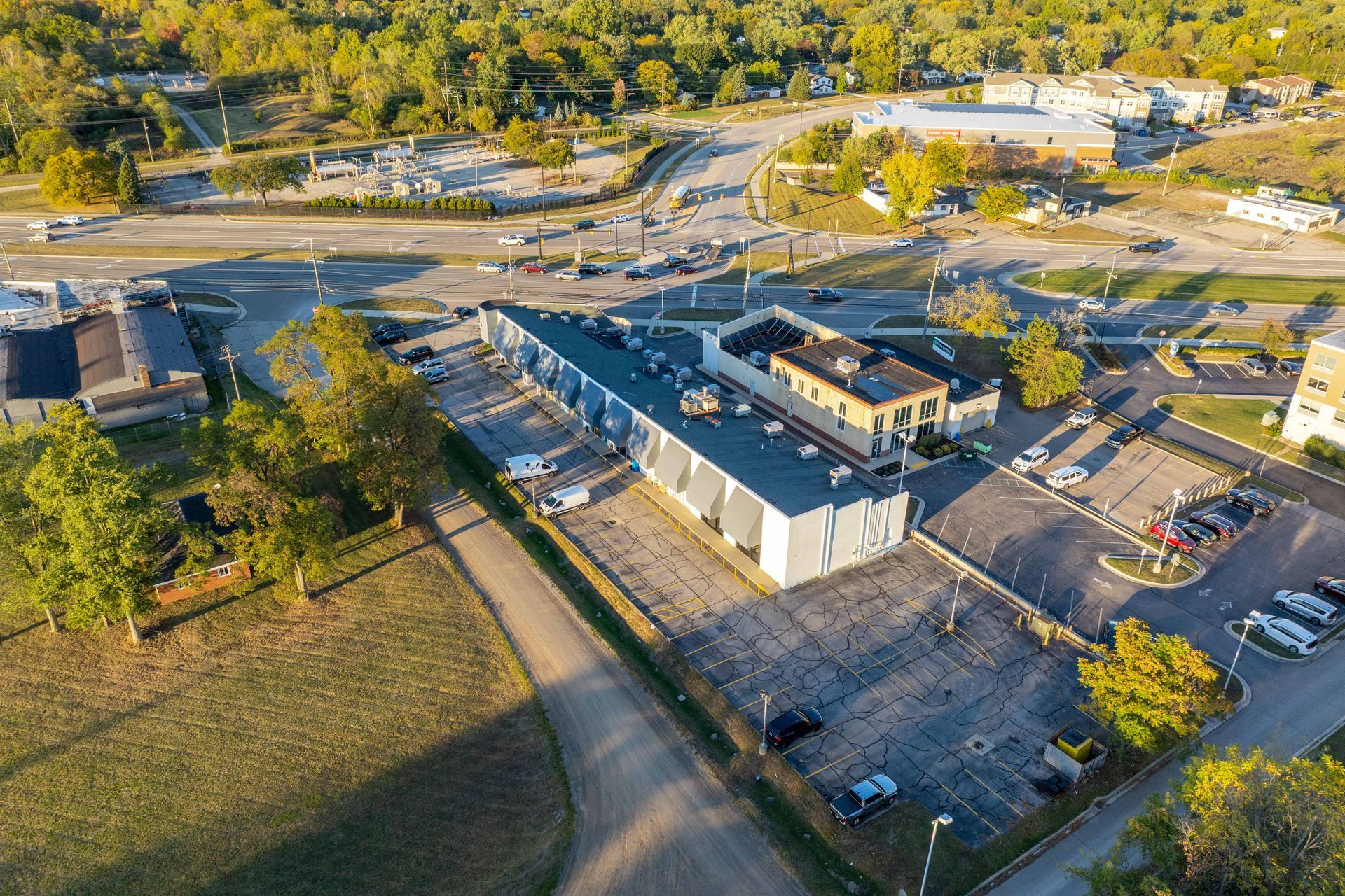 Aerial view of a large building with a parking lot, near a highway and trees.