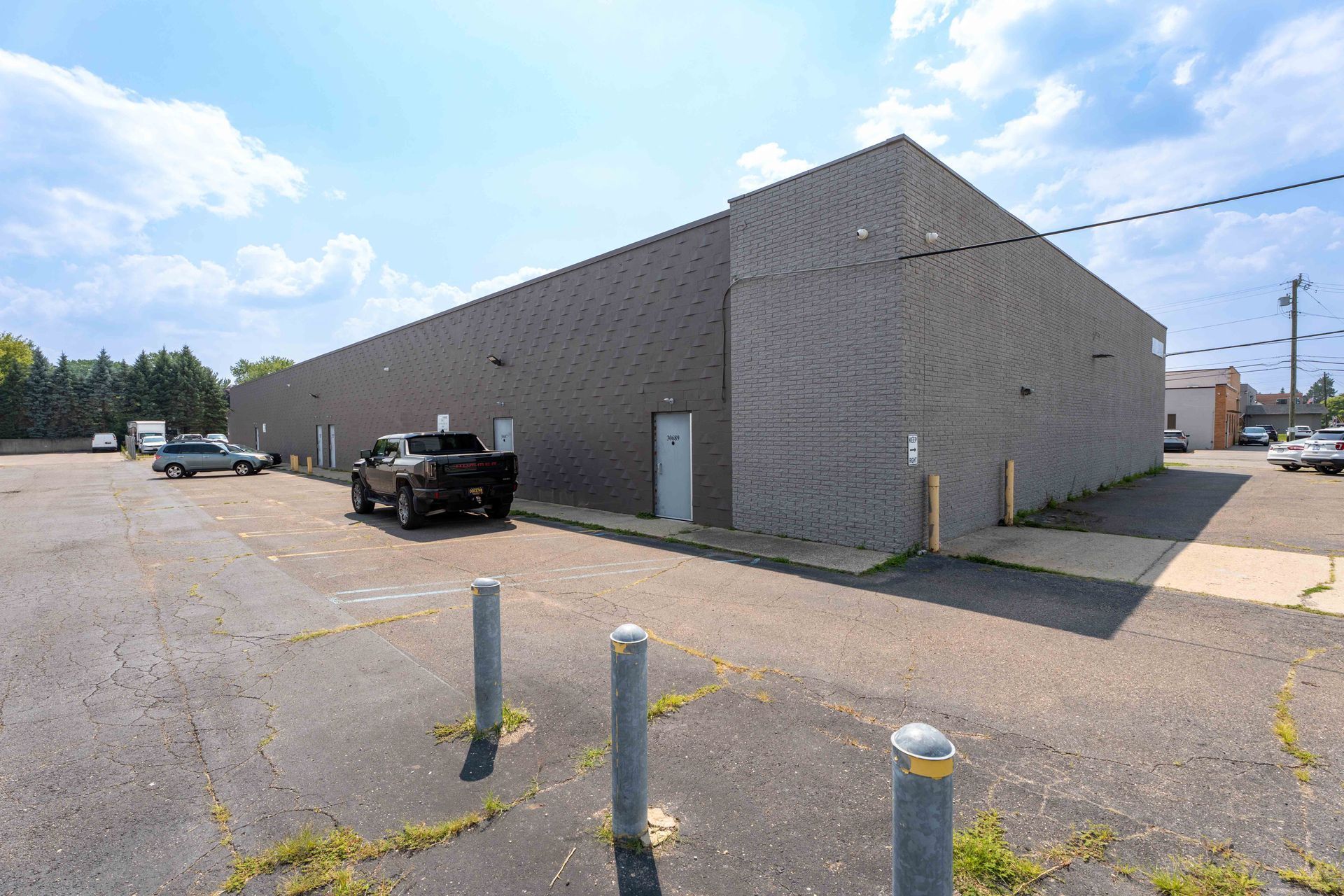 Gray industrial building with a paved parking area and several vehicles. Blue sky.