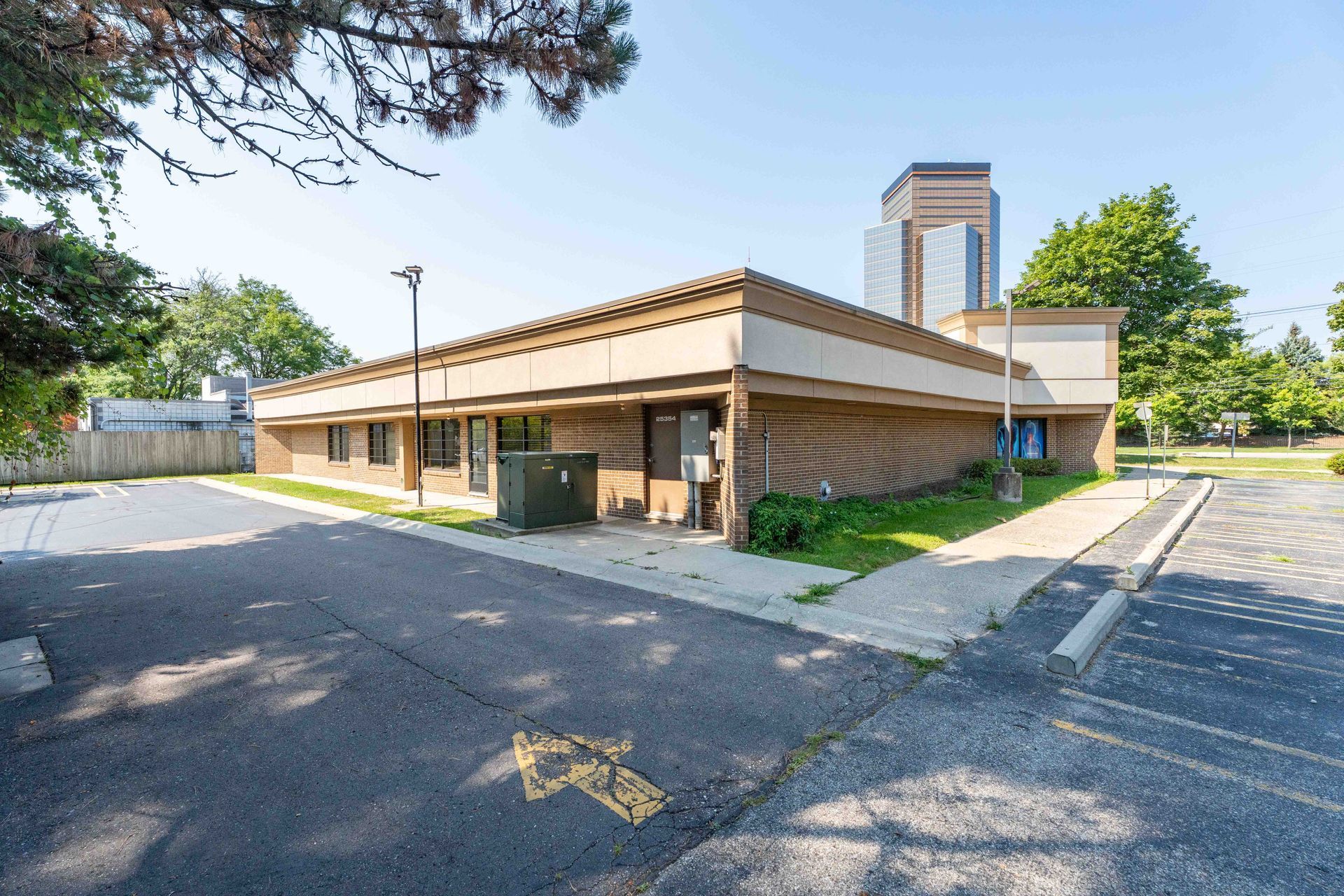 Brick building with parking lot and arrow. Brown trim, glass windows, and green trees.