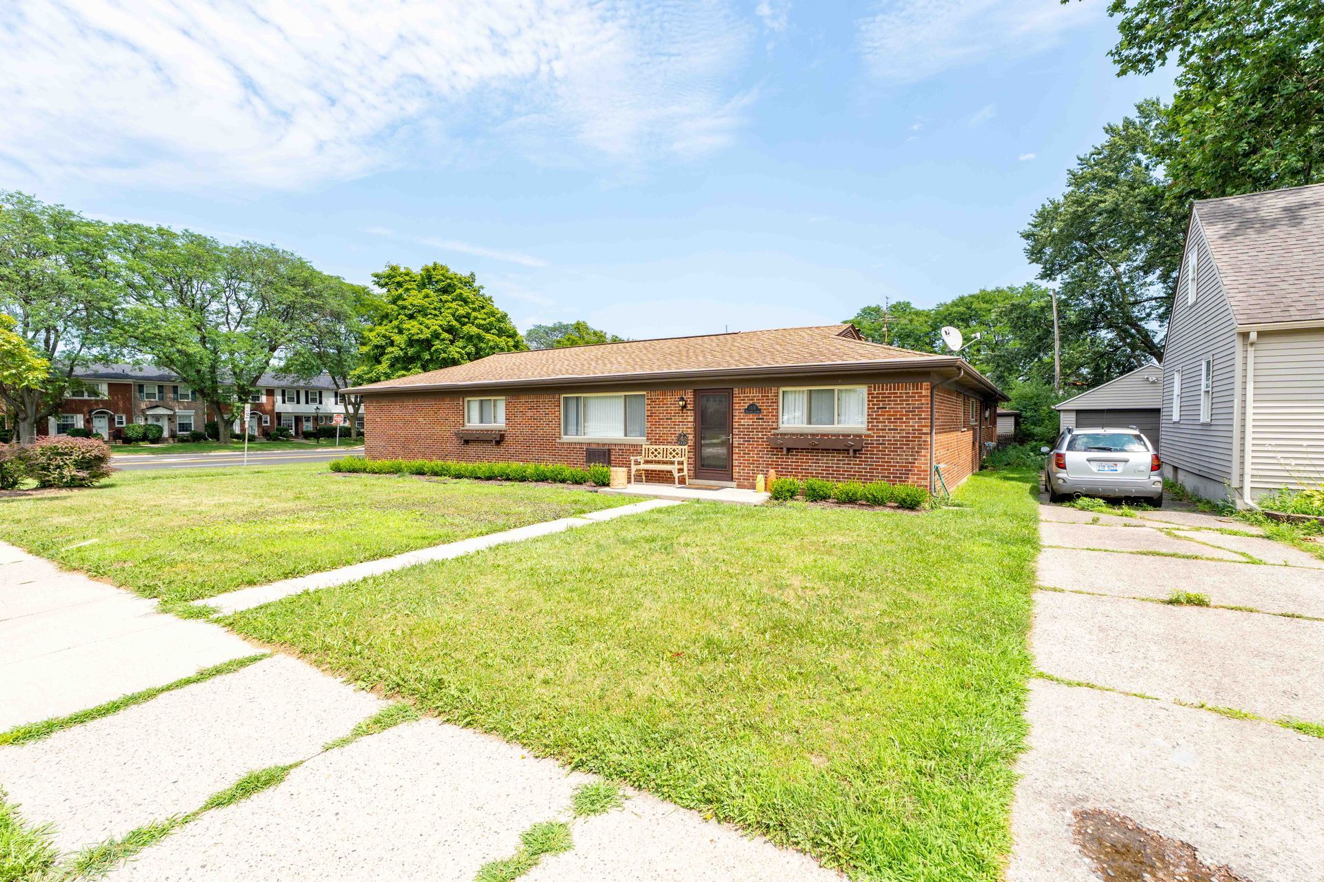 Brick ranch house with green lawn, driveway, and blue sky.