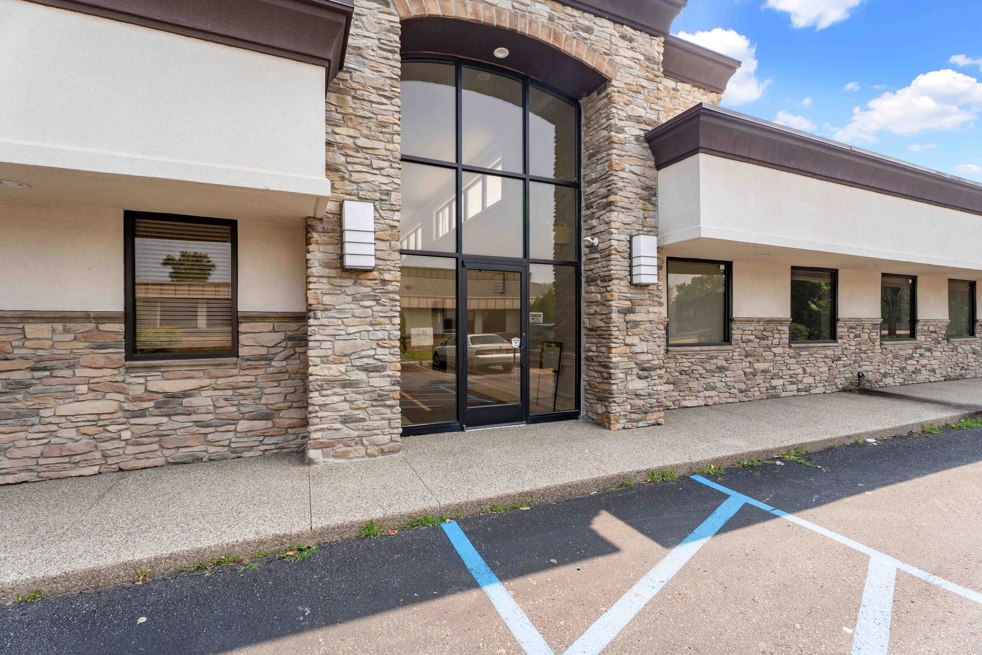 Building exterior with stone and brown trim, large glass doors, and windows; blue parking space markings.