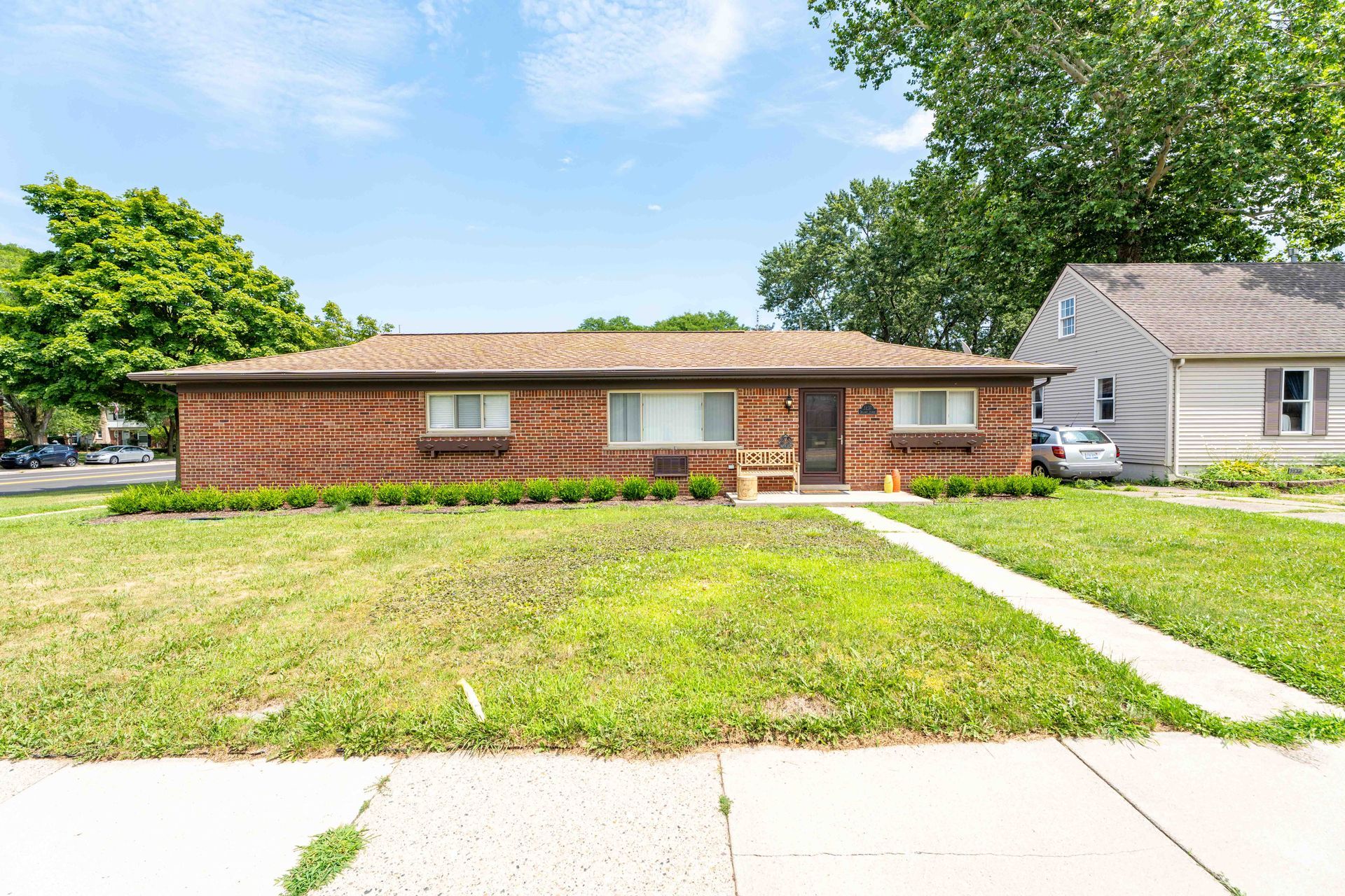 Brick ranch house with green lawn, shrubs, and a sidewalk leading to the front door on a sunny day.