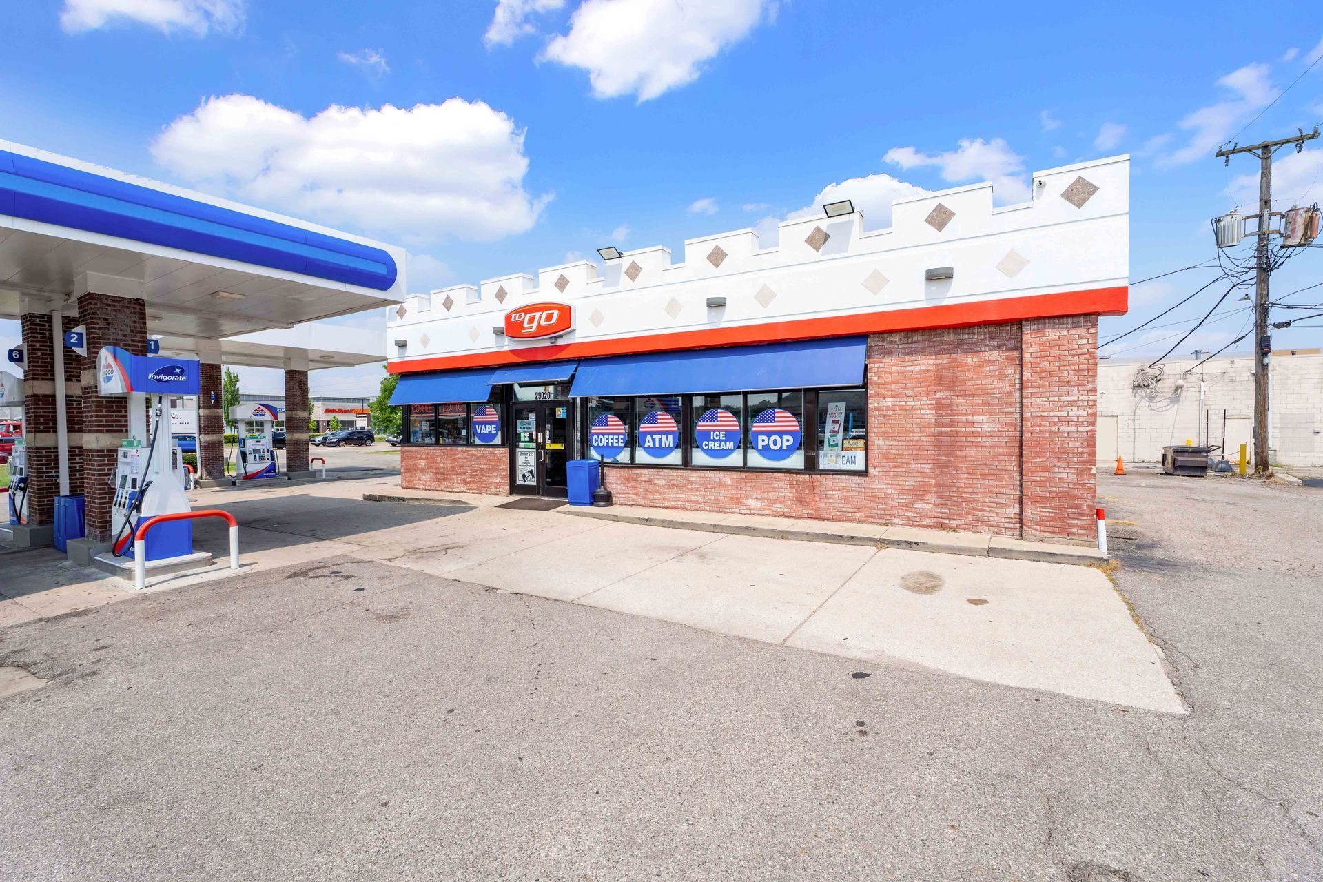 Gas station with a brick facade and blue canopy under a bright blue sky.
