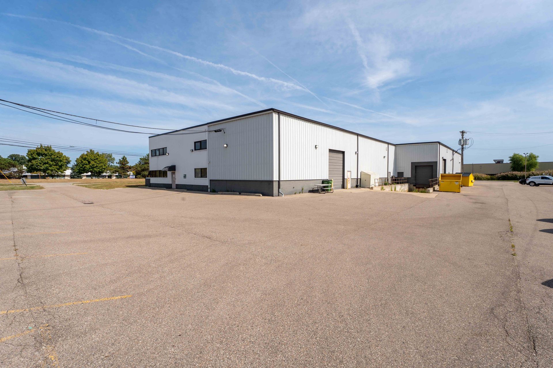 White industrial building with gray trim and paved lot under a blue sky.