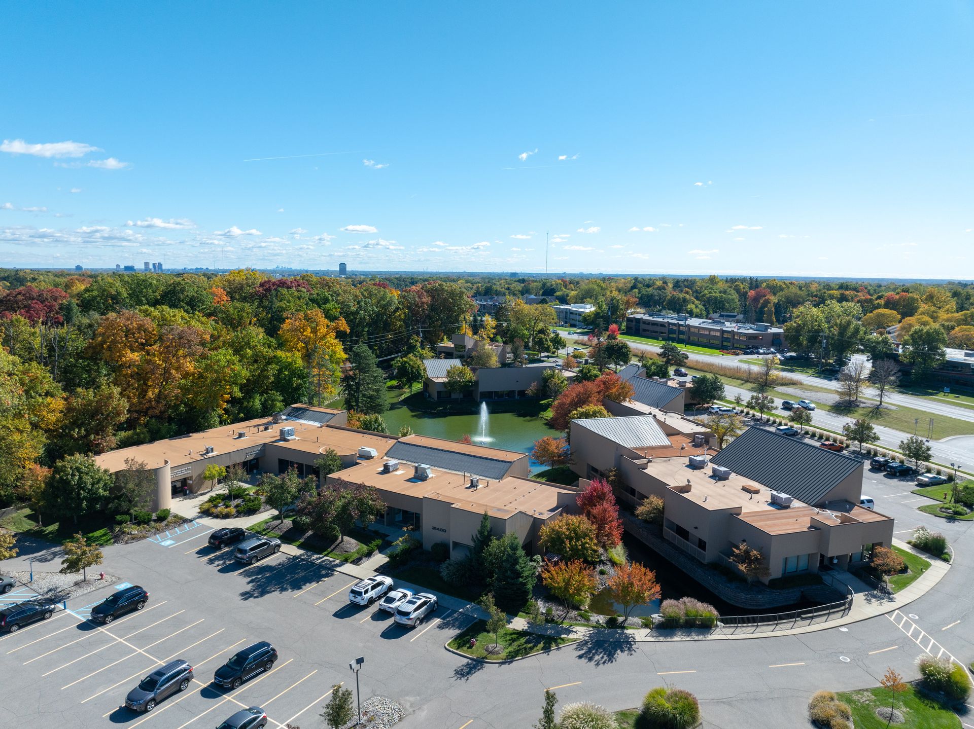 Aerial view of a building with a pond, surrounded by trees with fall colors and a parking lot.