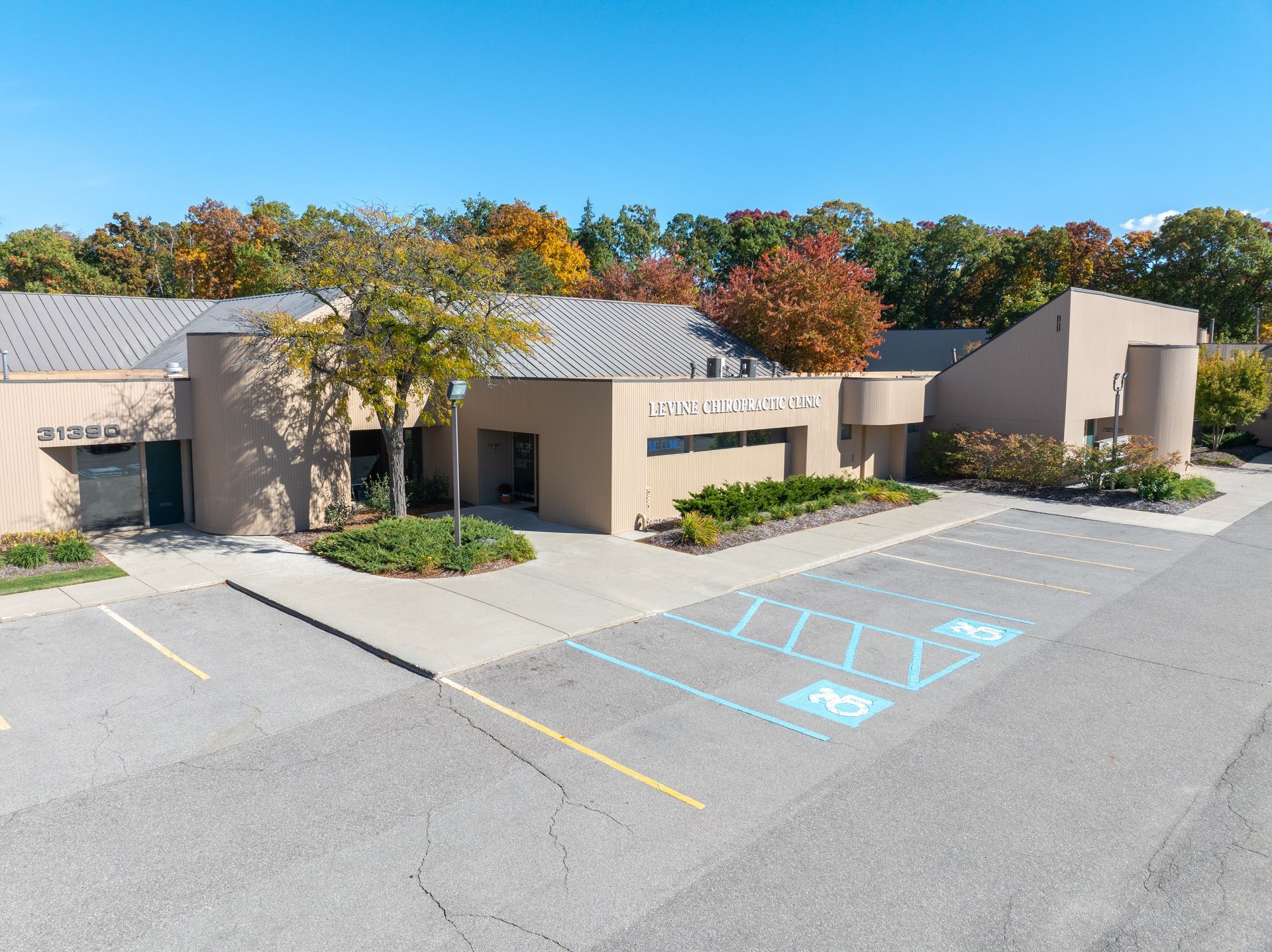 Exterior view of a beige building with accessibility parking spots. Autumn trees in the background.