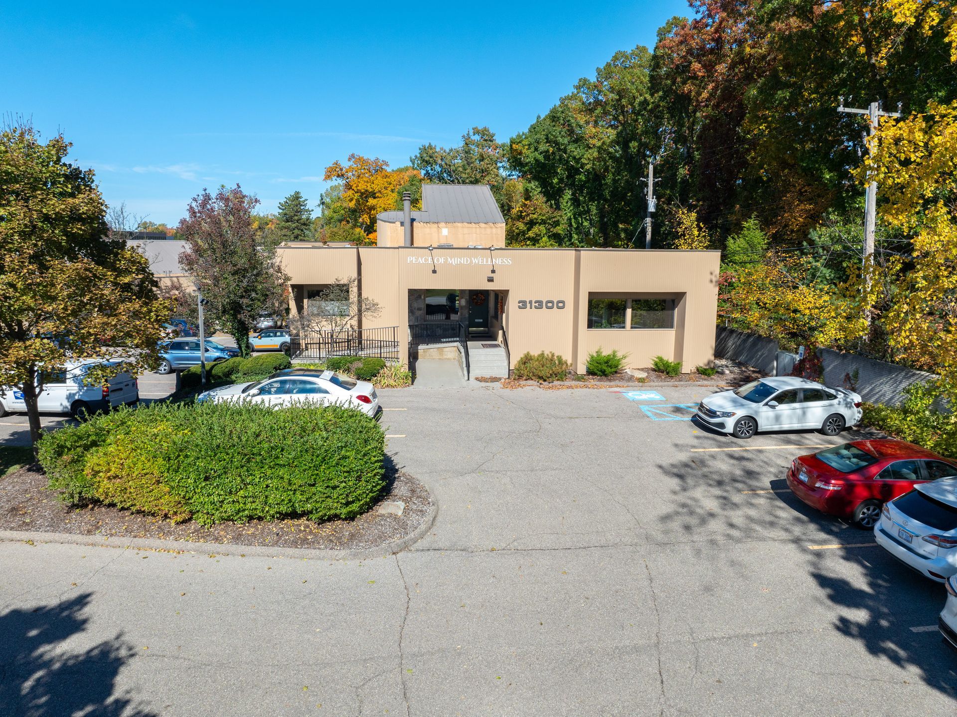 Exterior view of a beige building with a parking lot, cars, and surrounding trees under a blue sky.