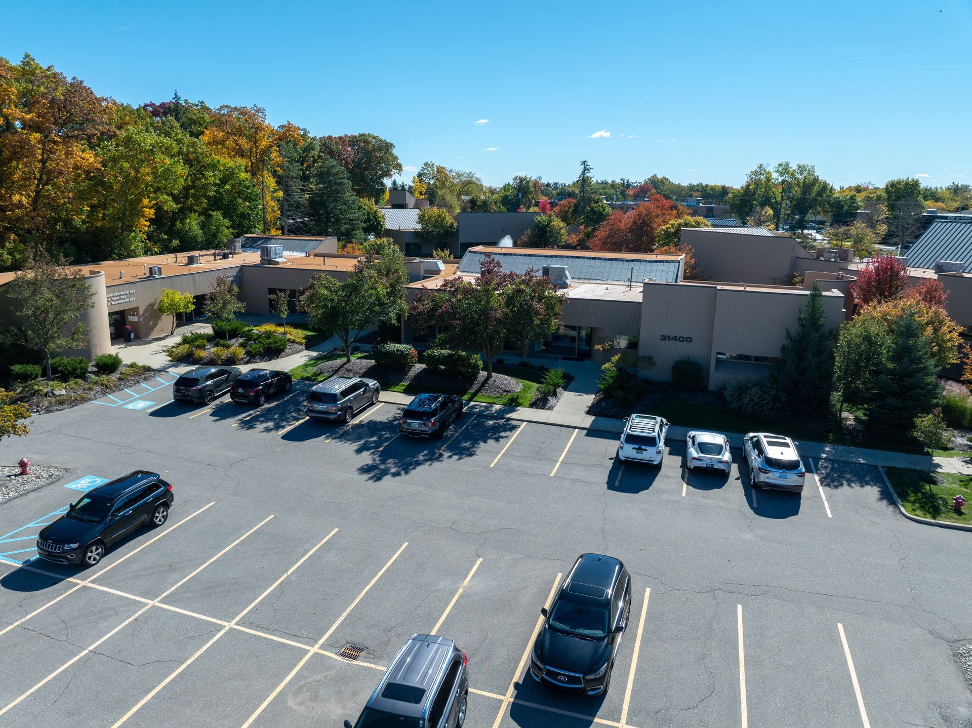 Parking lot with cars in front of a building surrounded by trees with fall foliage.