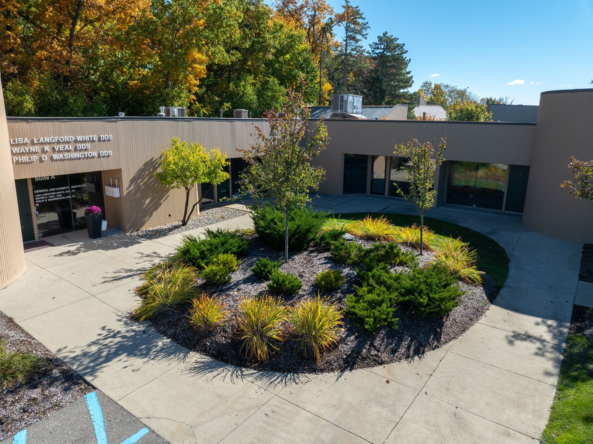 Exterior of a brick building with a landscaped courtyard; trees with fall foliage and blue parking space.