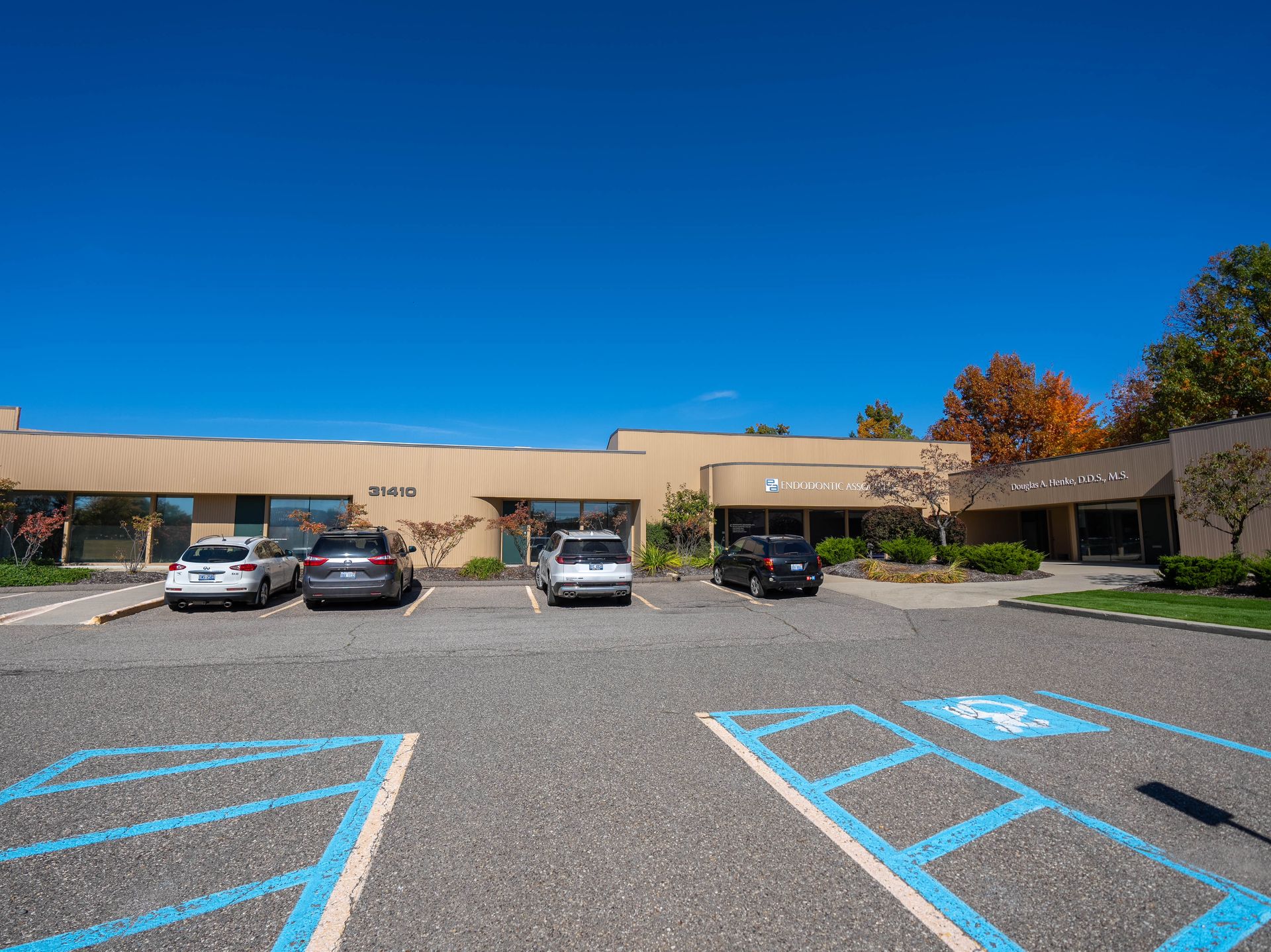 Exterior view of a beige building with cars parked in front and a clear blue sky overhead.