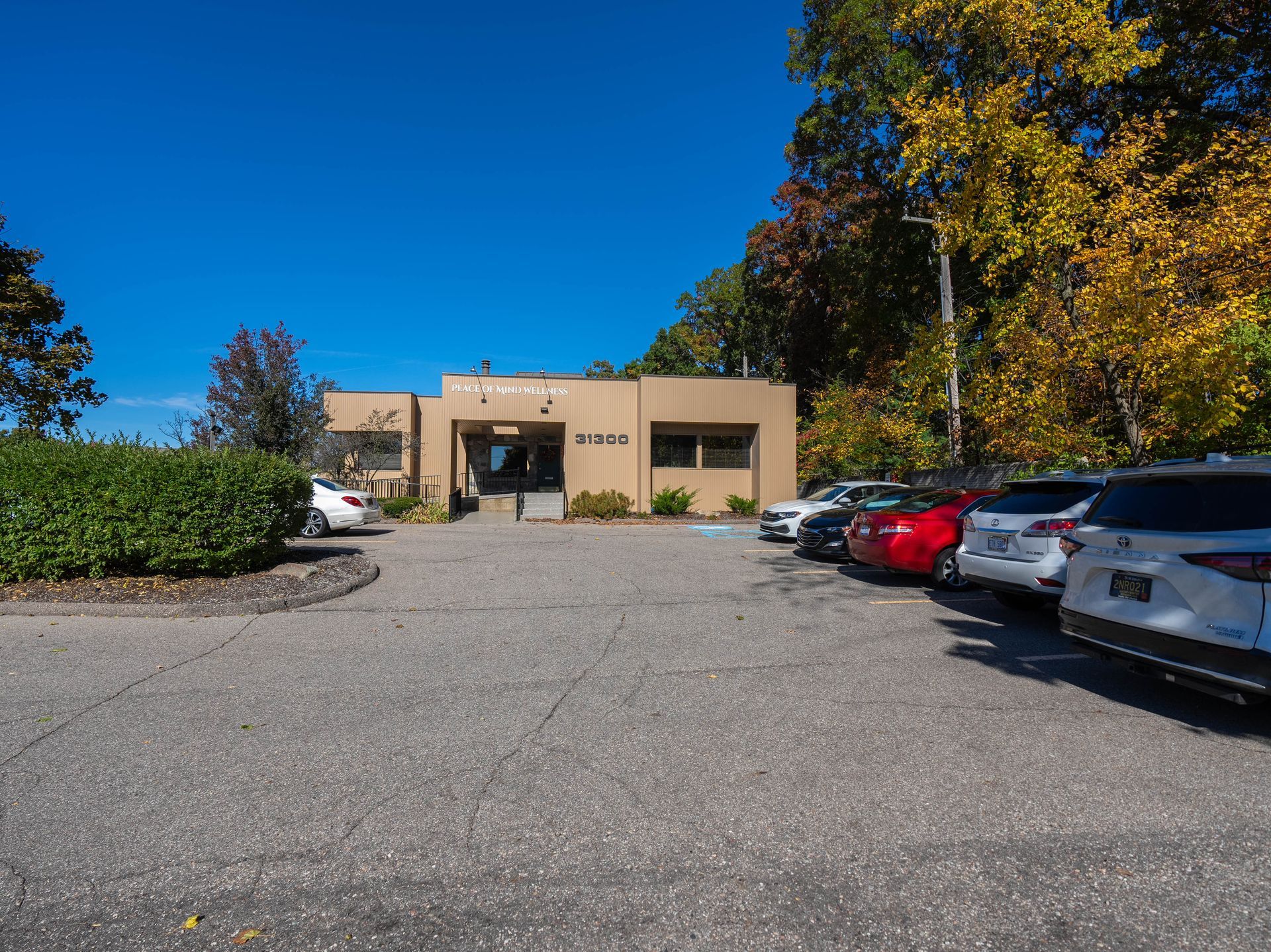 Building with parked cars in front, trees with fall foliage, and a clear blue sky.